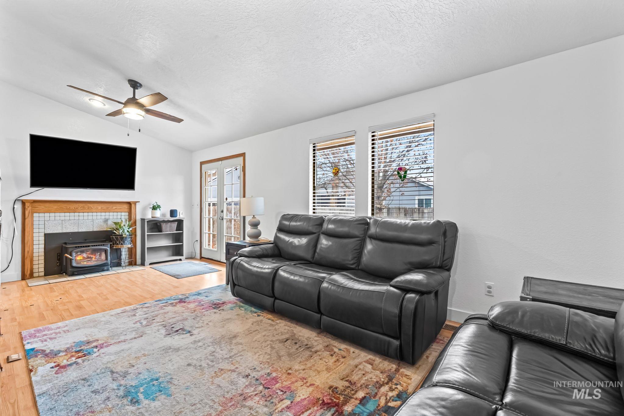 Living room with a wood stove, lofted ceiling, light wood-type flooring, a textured ceiling, and ceiling fan