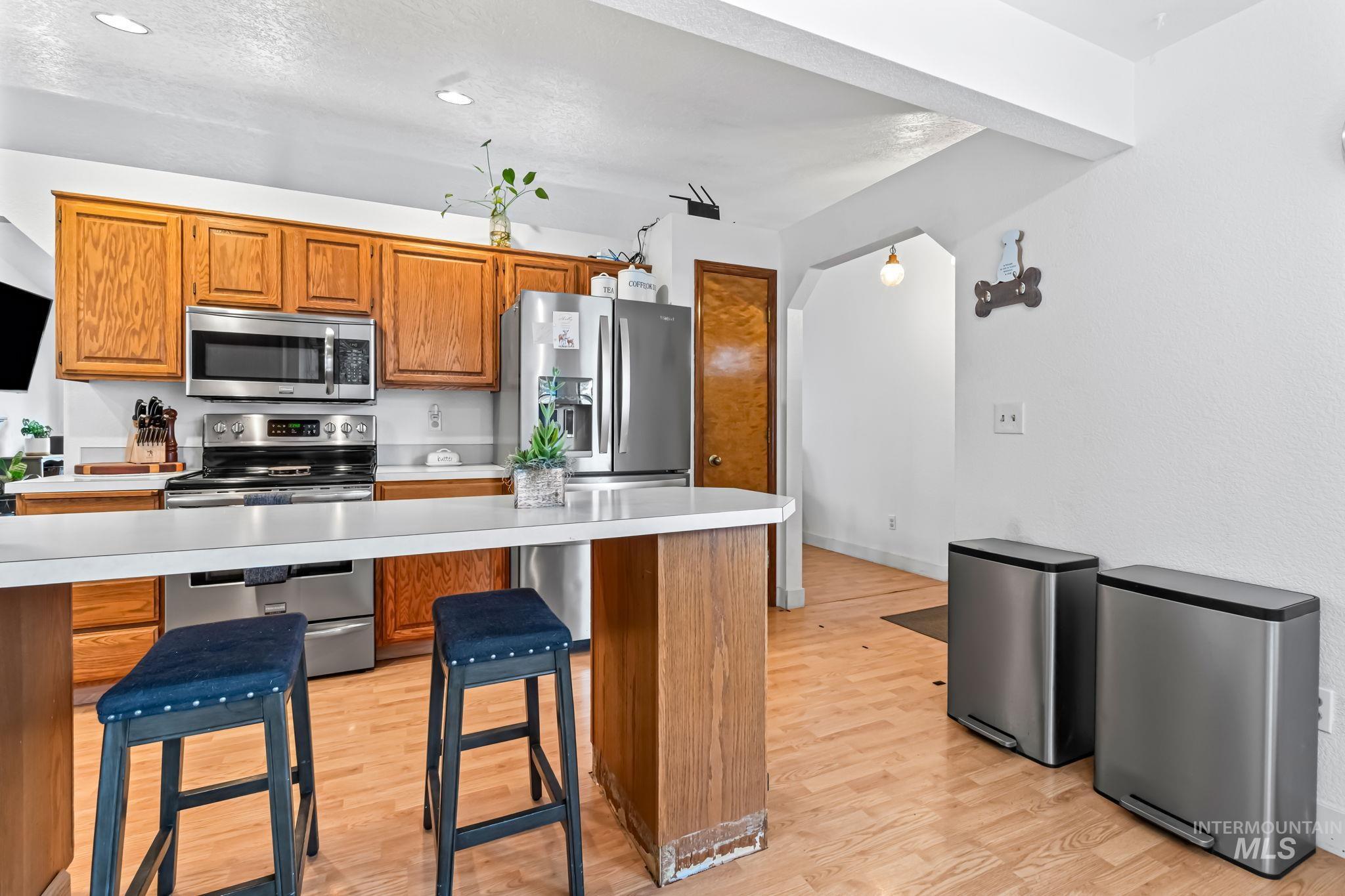 Kitchen with light countertops, appliances with stainless steel finishes, a kitchen bar, and brown cabinets