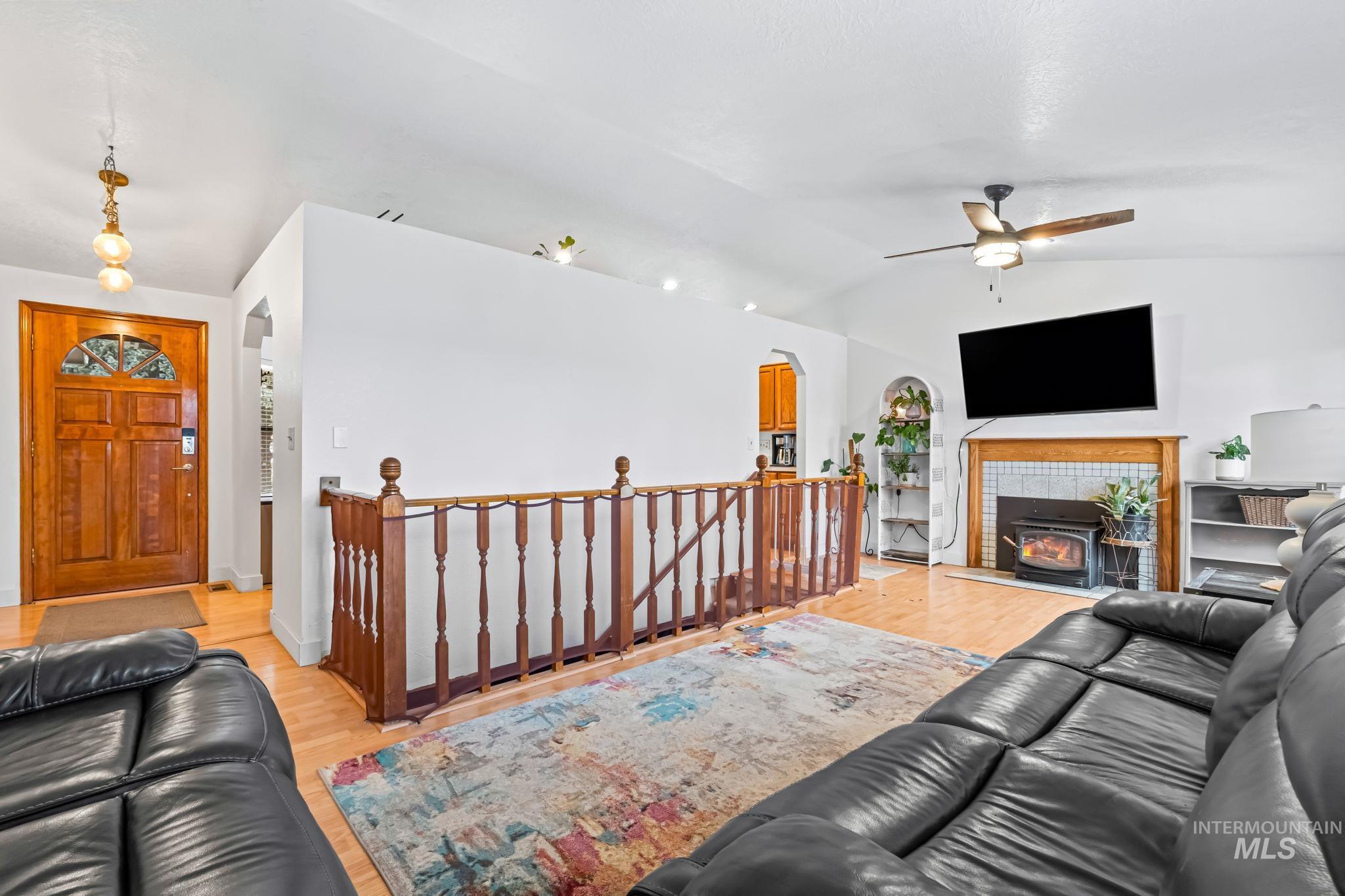 Living area featuring light wood finished floors, arched walkways, lofted ceiling, ceiling fan, and a tiled fireplace