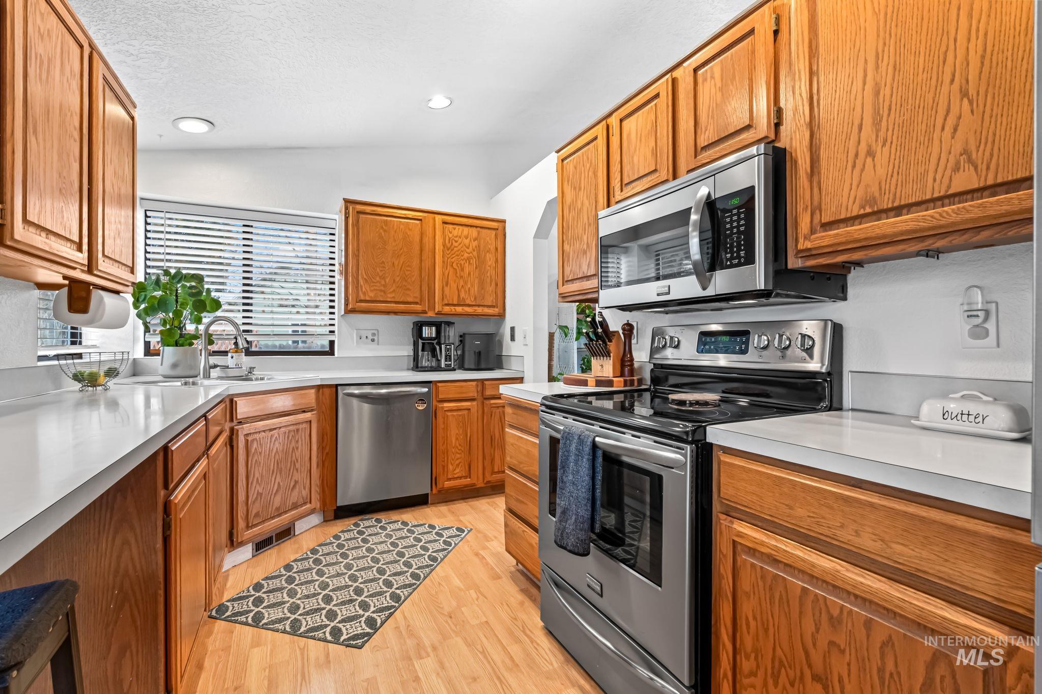 Kitchen with stainless steel appliances, lofted ceiling, brown cabinetry, light countertops, and light wood-style floors