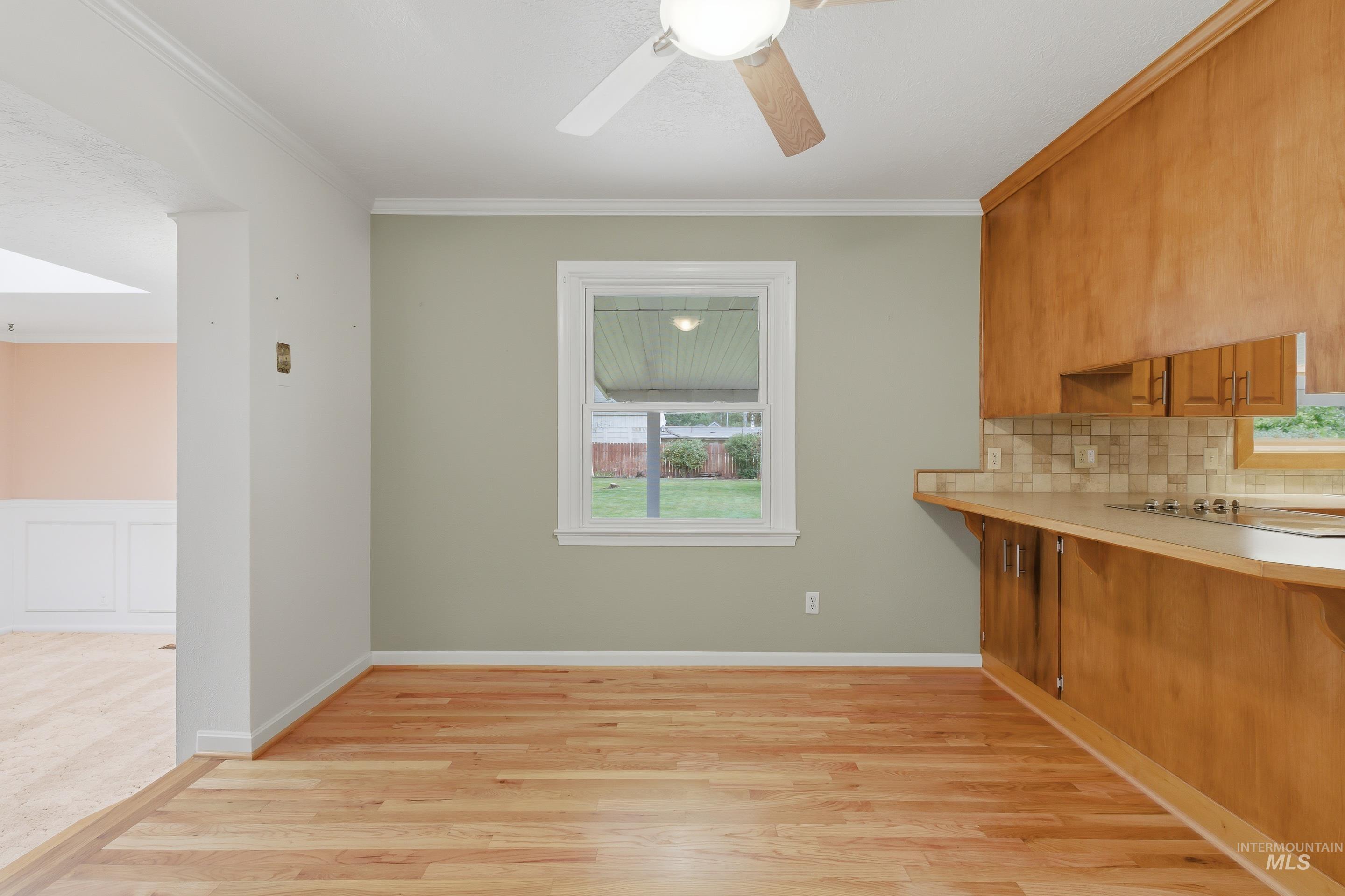 Open concept space featuring wood-finish flooring, a ceiling fan, and a kitchen area with wood cabinetry, a tiled backsplash, and light countertops