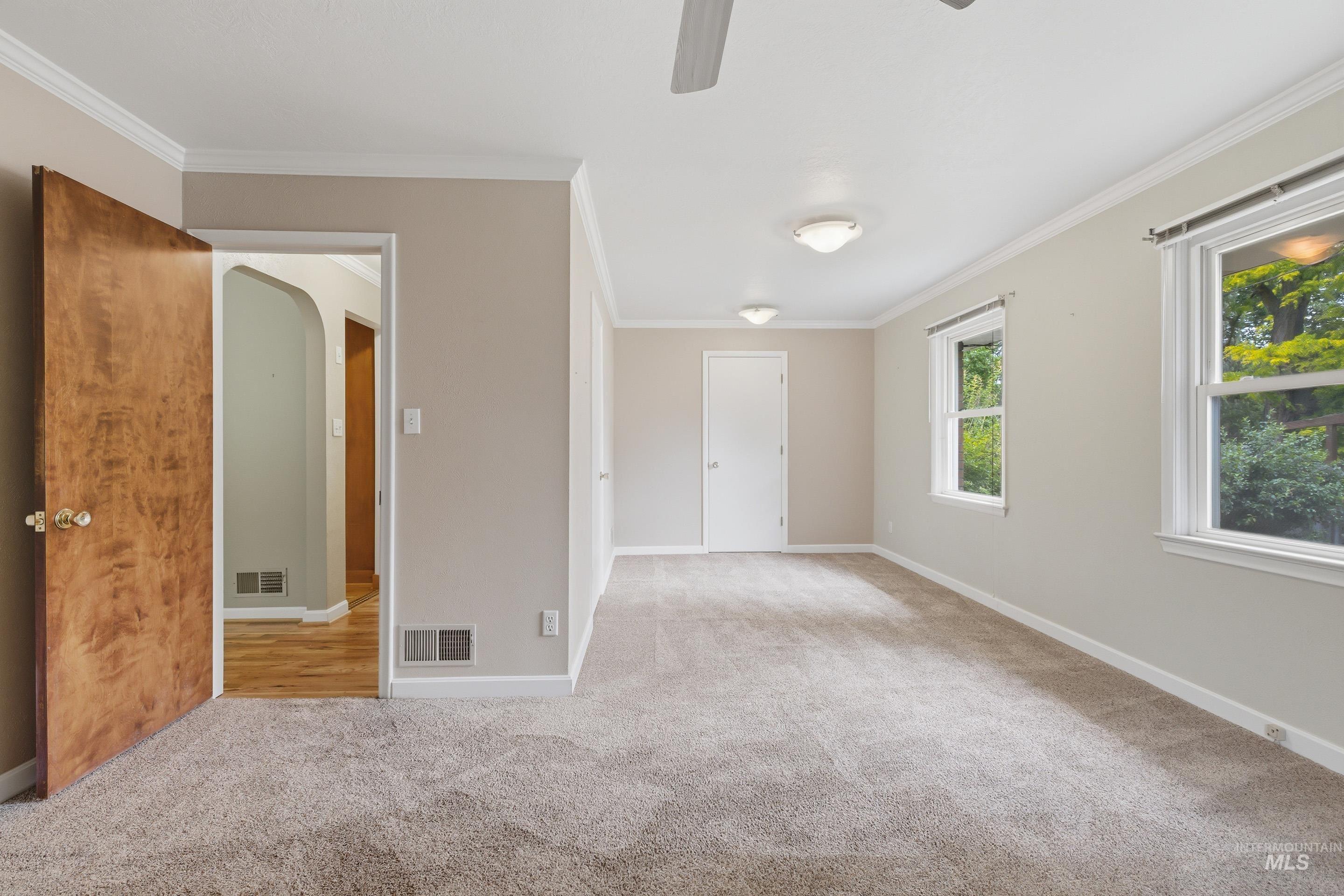 Spacious room featuring neutral carpeting, crown molding, double windows, a ceiling fan, and two flush-mount light fixtures