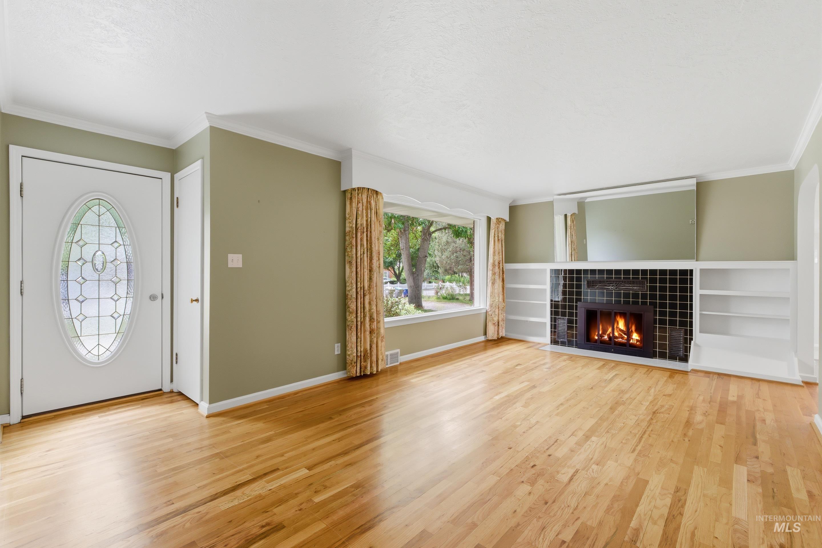 Spacious living area featuring light wood flooring, a fireplace with black tile surround, and built-in shelving