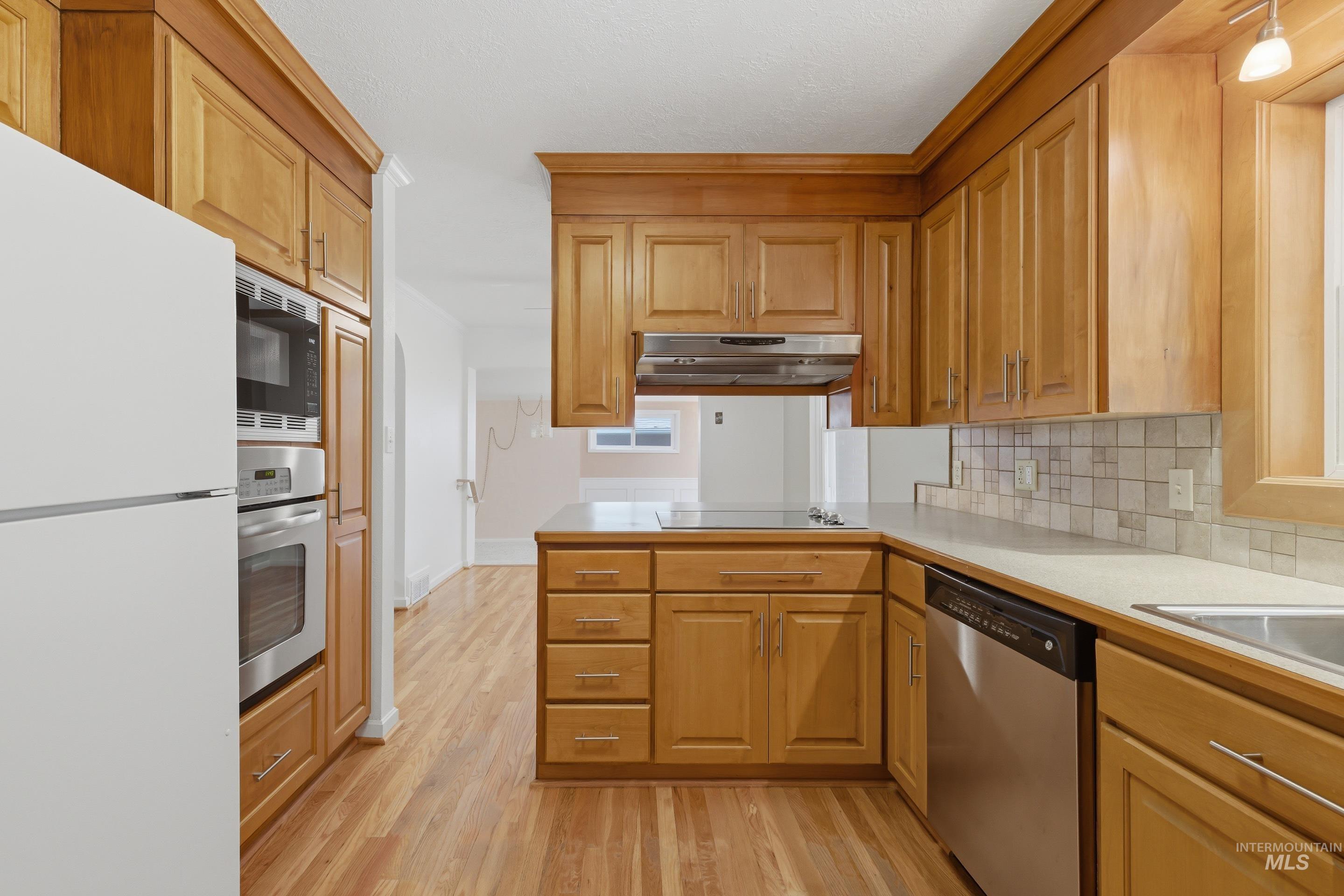 Kitchen featuring wood-finish cabinetry, stainless steel appliances, a built-in oven and microwave, and a tile backsplash