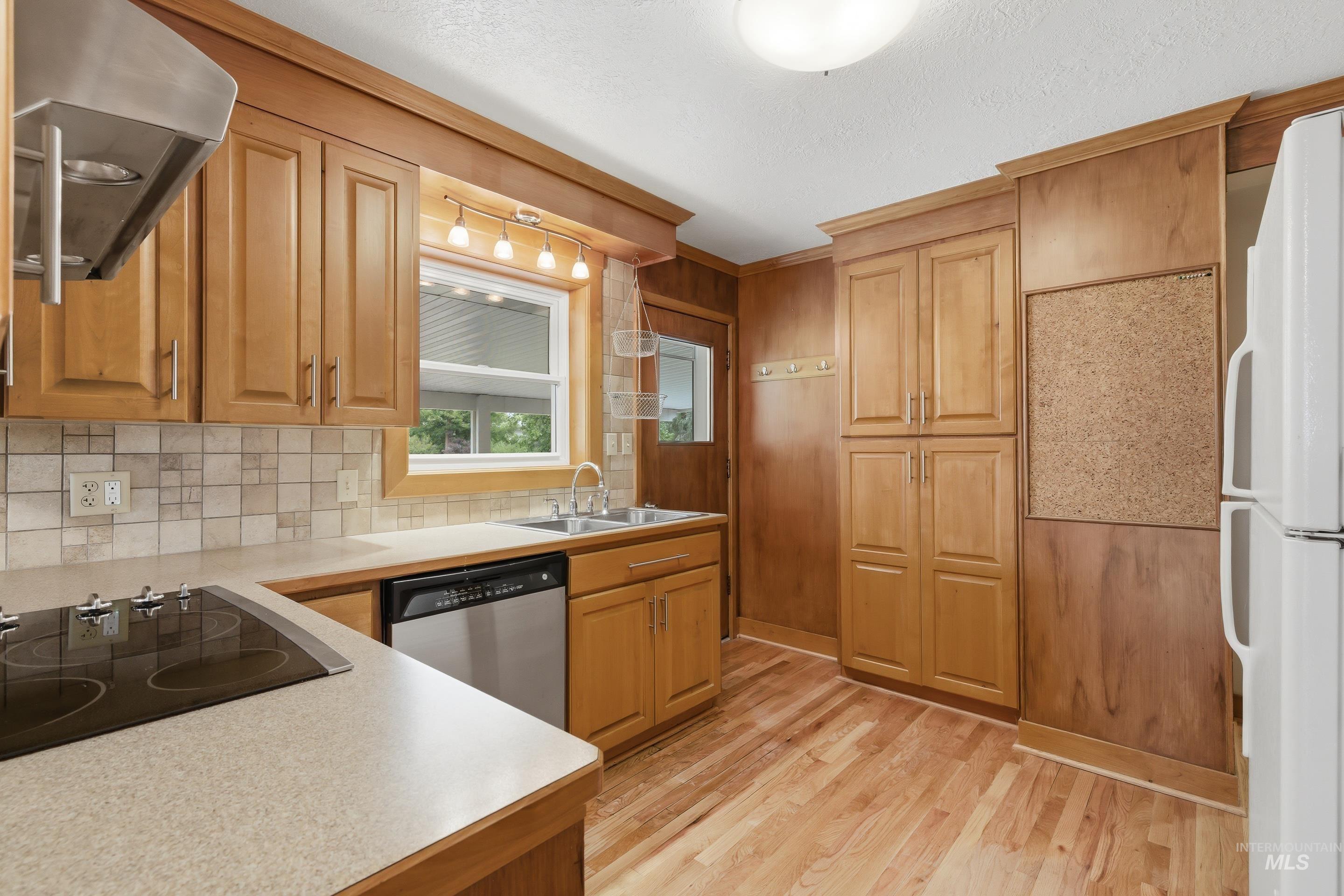 Kitchen featuring wood-finish flooring, wood cabinetry, a built-in dishwasher, and a stainless steel range hood