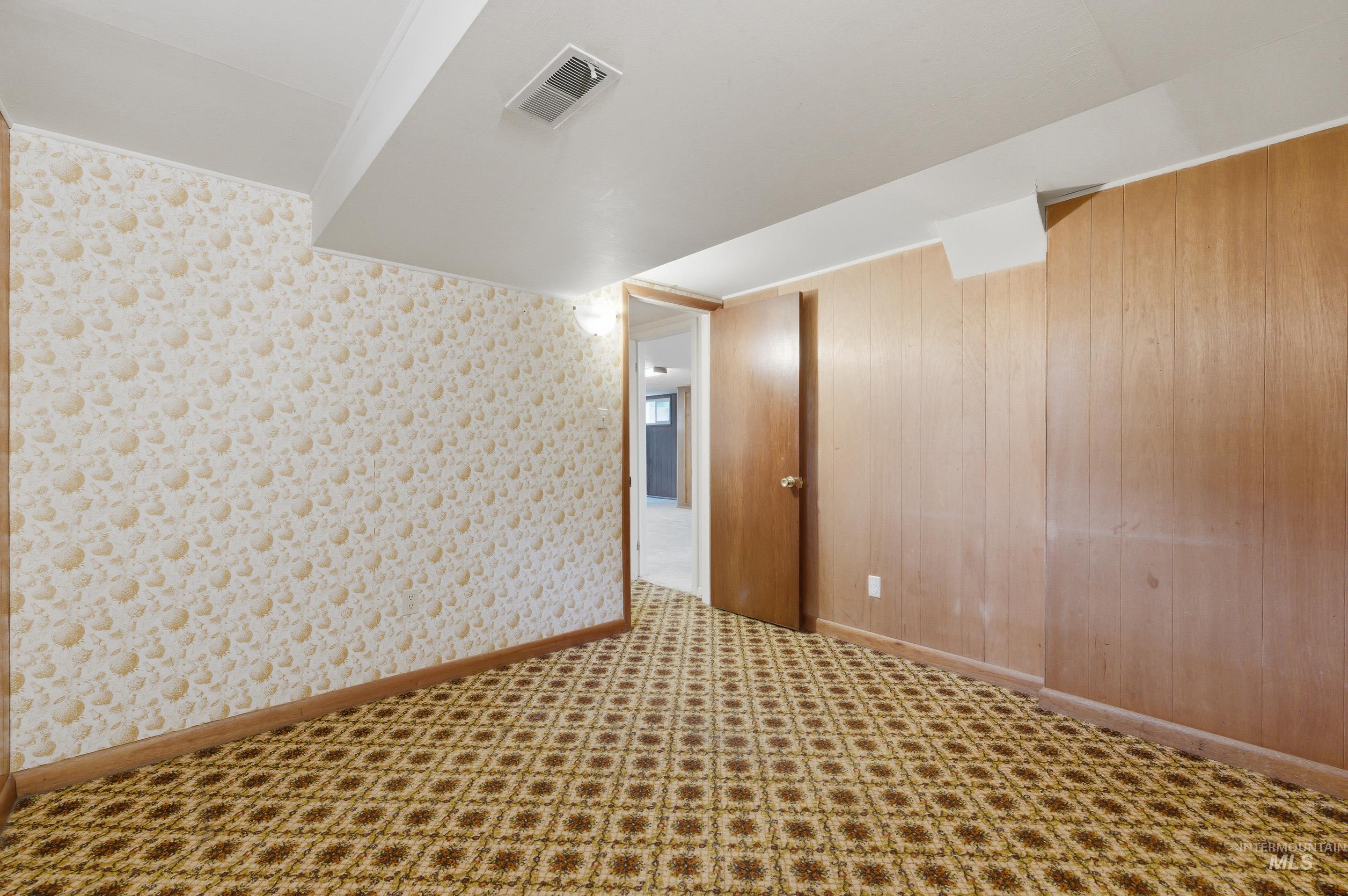 Room with patterned carpet flooring, a light-colored accent wall with subtle patterning, and wood paneling on the opposing wall