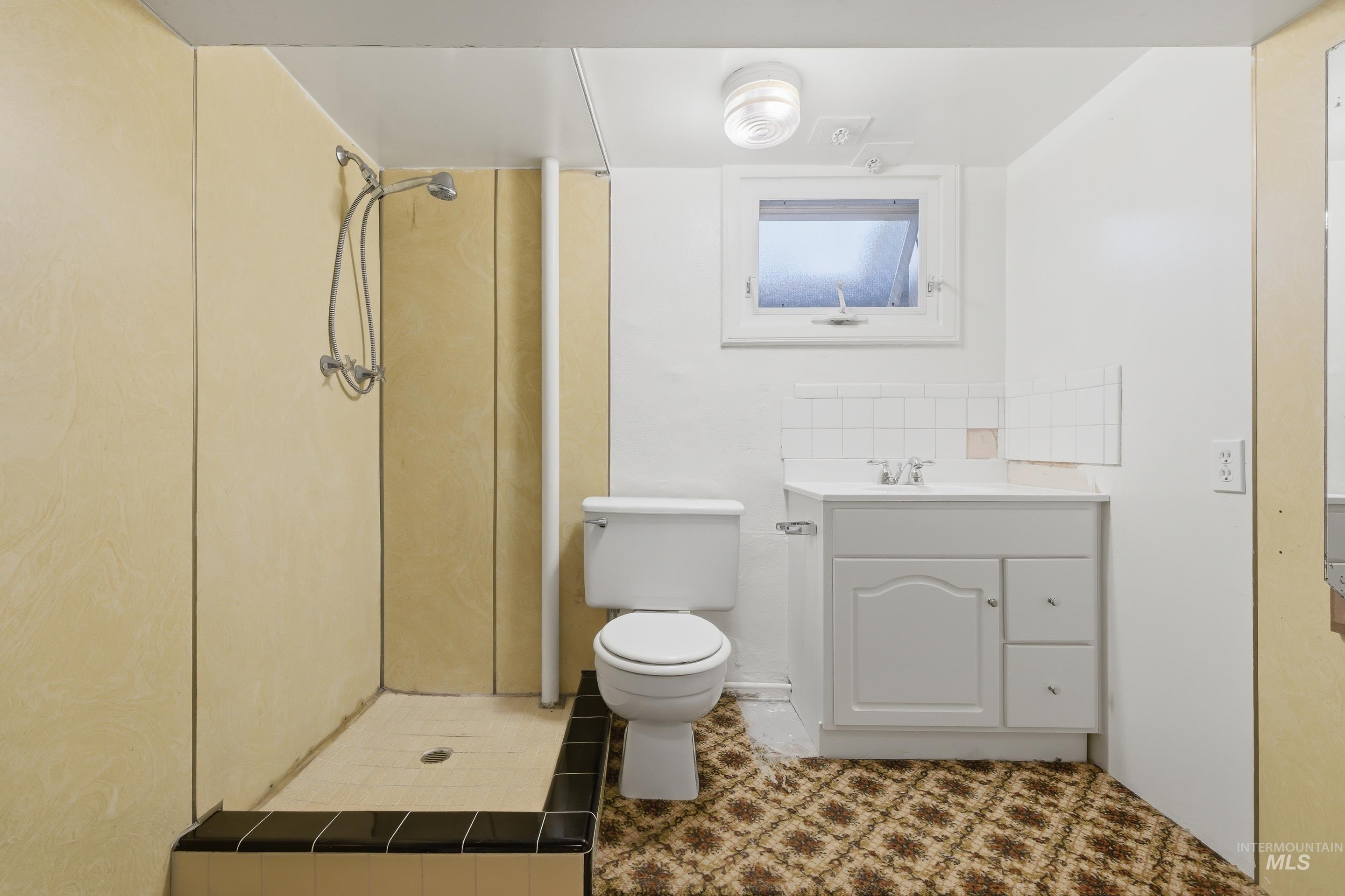 Bathroom featuring a white vanity with integrated sink, a toilet, and a tiled shower base with black trim