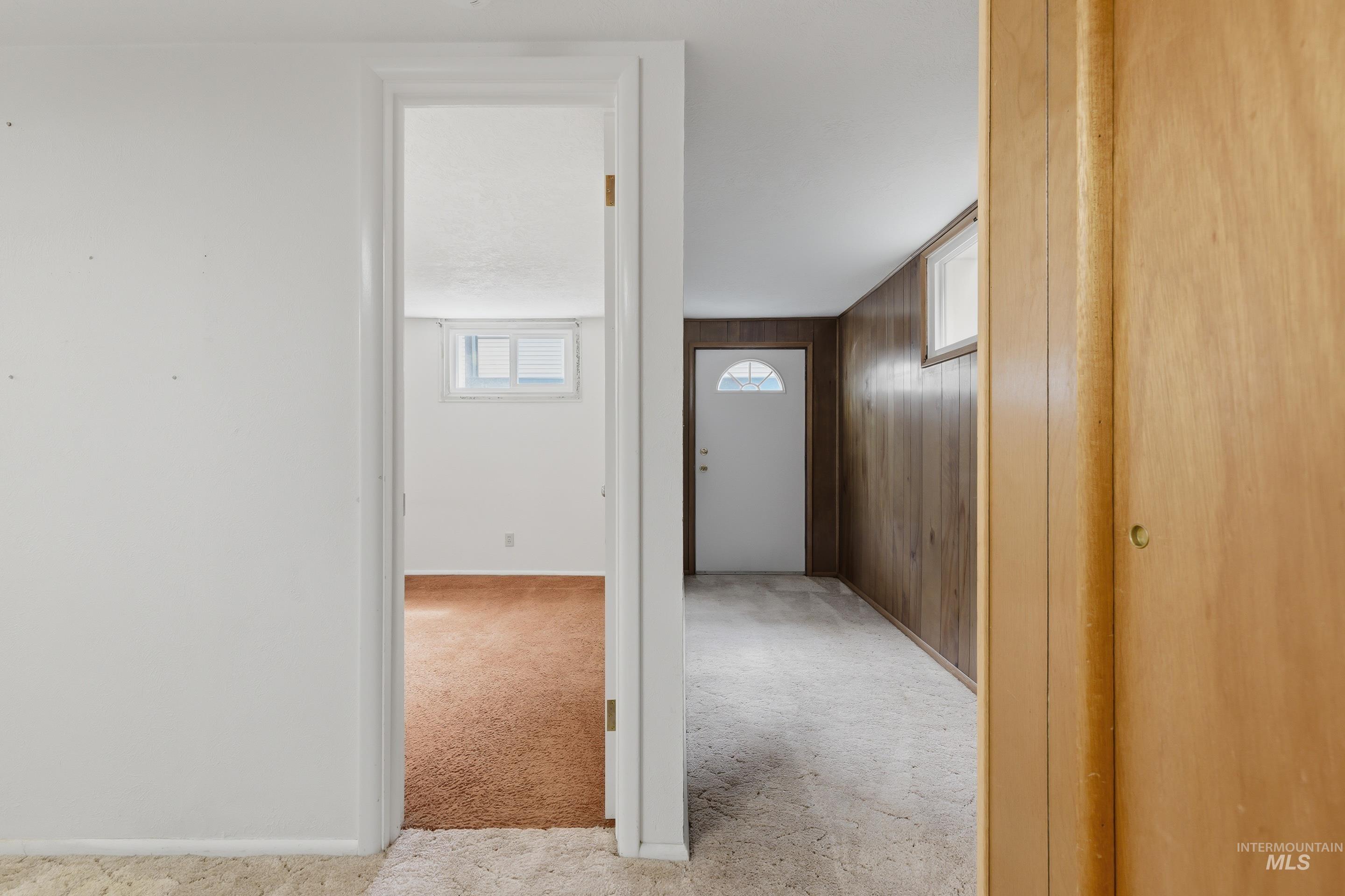Interior hallway with light wood paneling, white door with arched glass insert, and light-colored carpeting