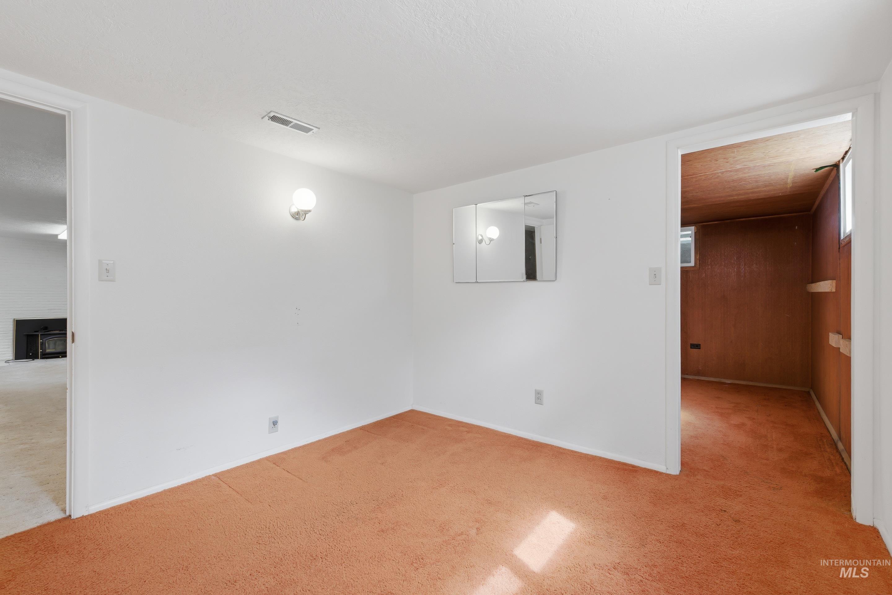 Carpeted room with white walls, wall-mounted light fixture, and a tri-fold medicine cabinet