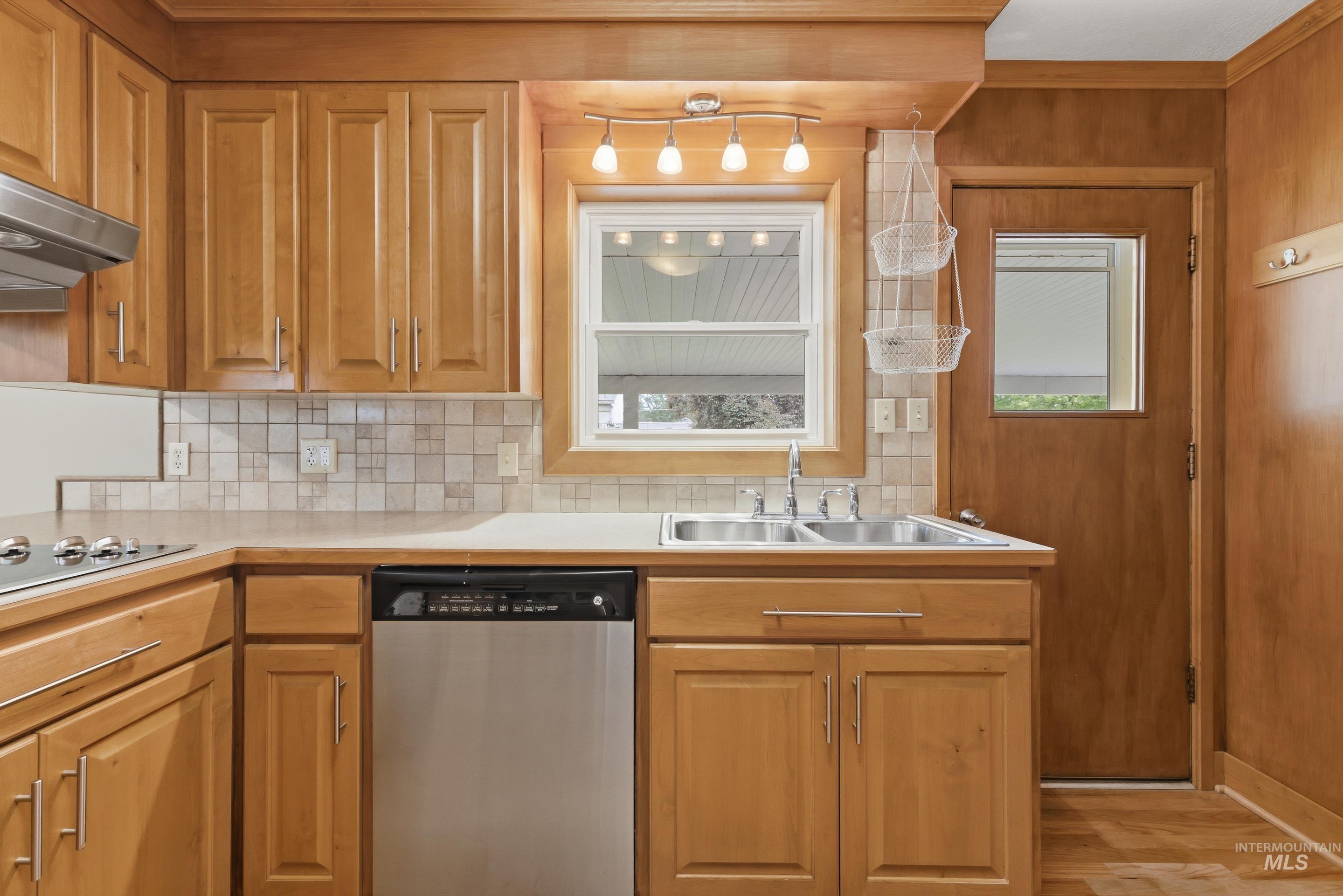 Kitchen featuring light wood cabinetry and paneling, a stainless steel dishwasher, and a double basin sink
