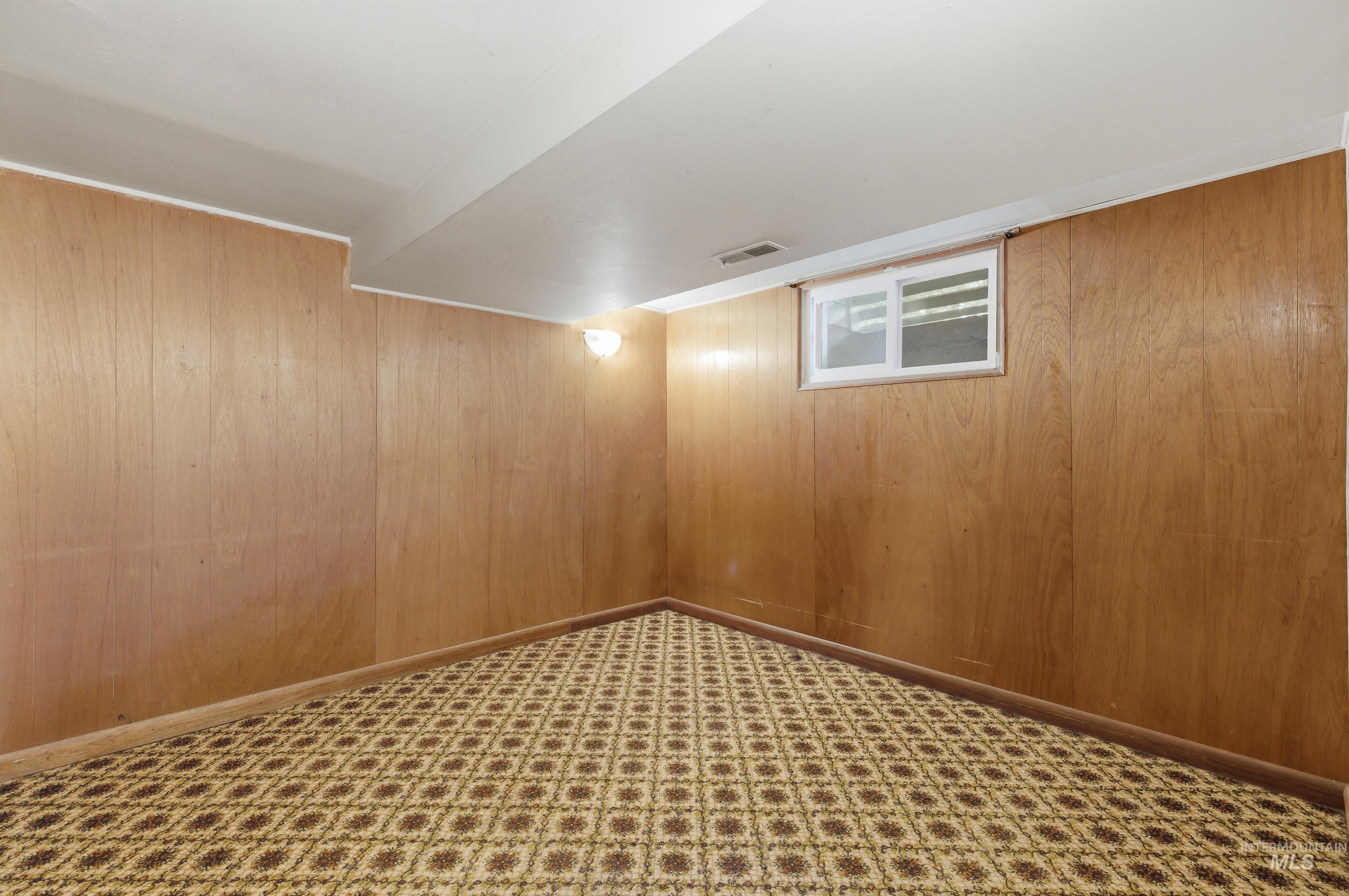 Room featuring wood paneling, a patterned carpet, a white ceiling, and a wall-mounted light fixture