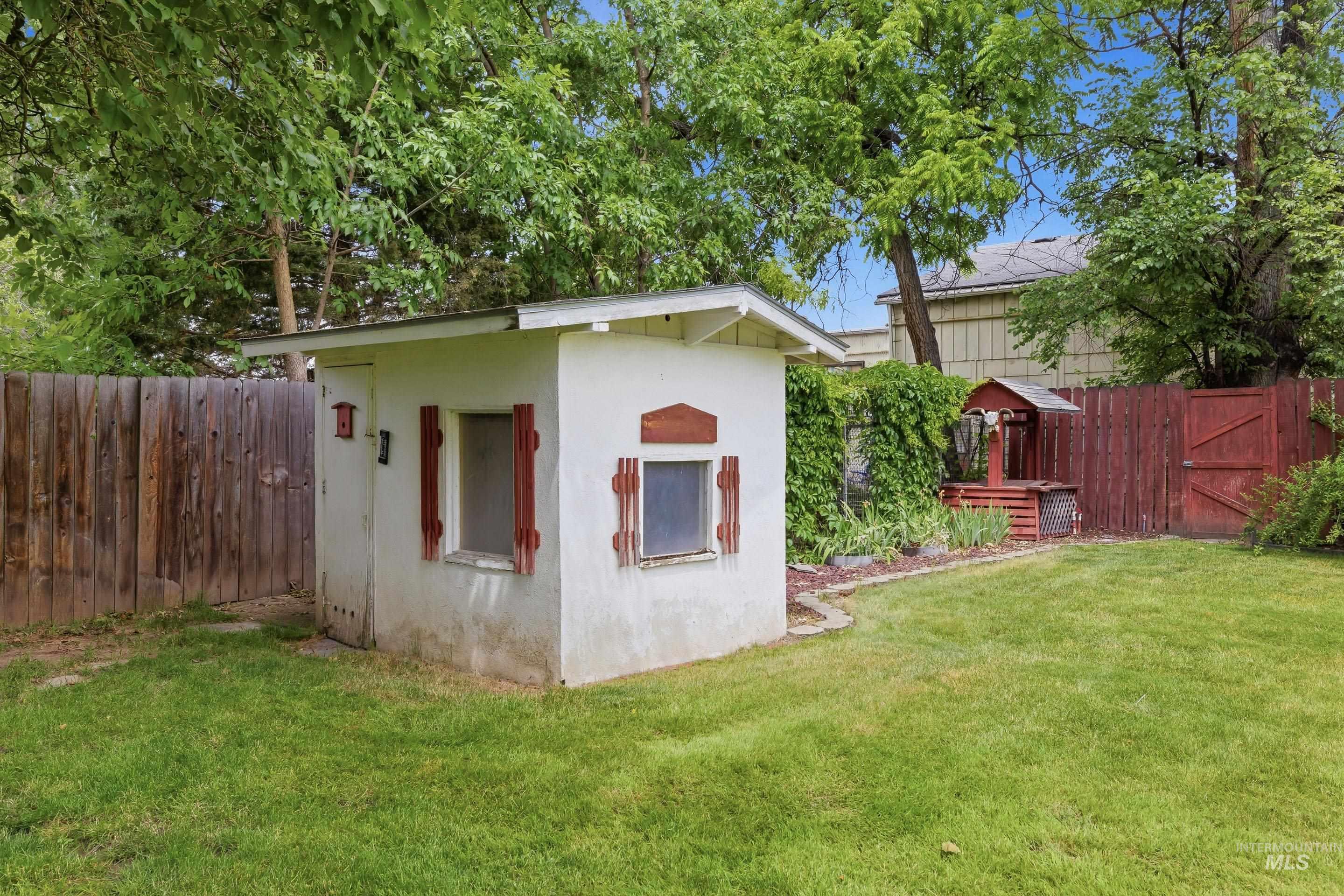 Backyard featuring a stucco utility shed with red shutters, wooden fencing, and a manicured lawn