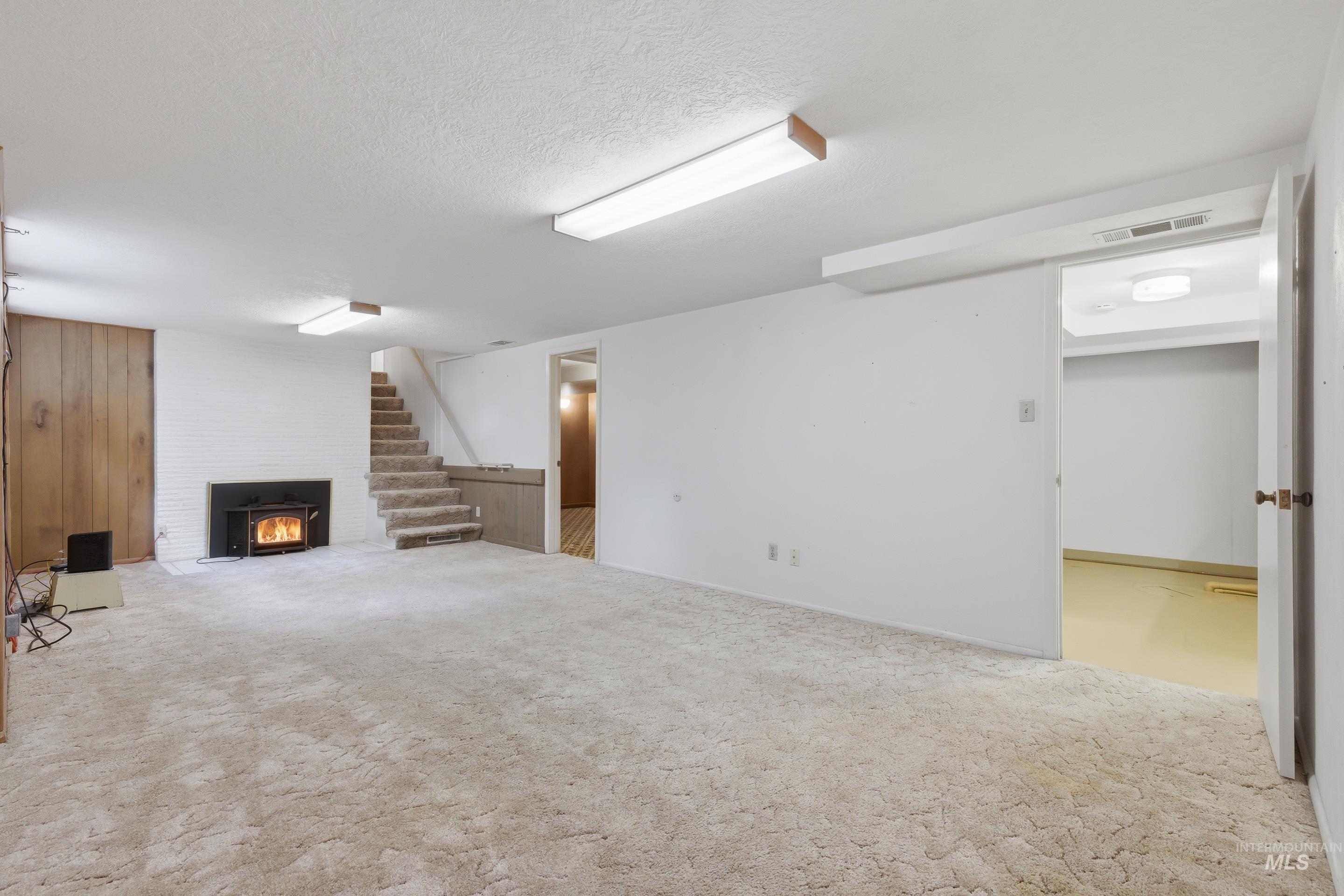 Spacious finished basement featuring a wood-burning fireplace insert with a painted brick surround, wood paneling accent wall, recessed lighting, and carpet flooring