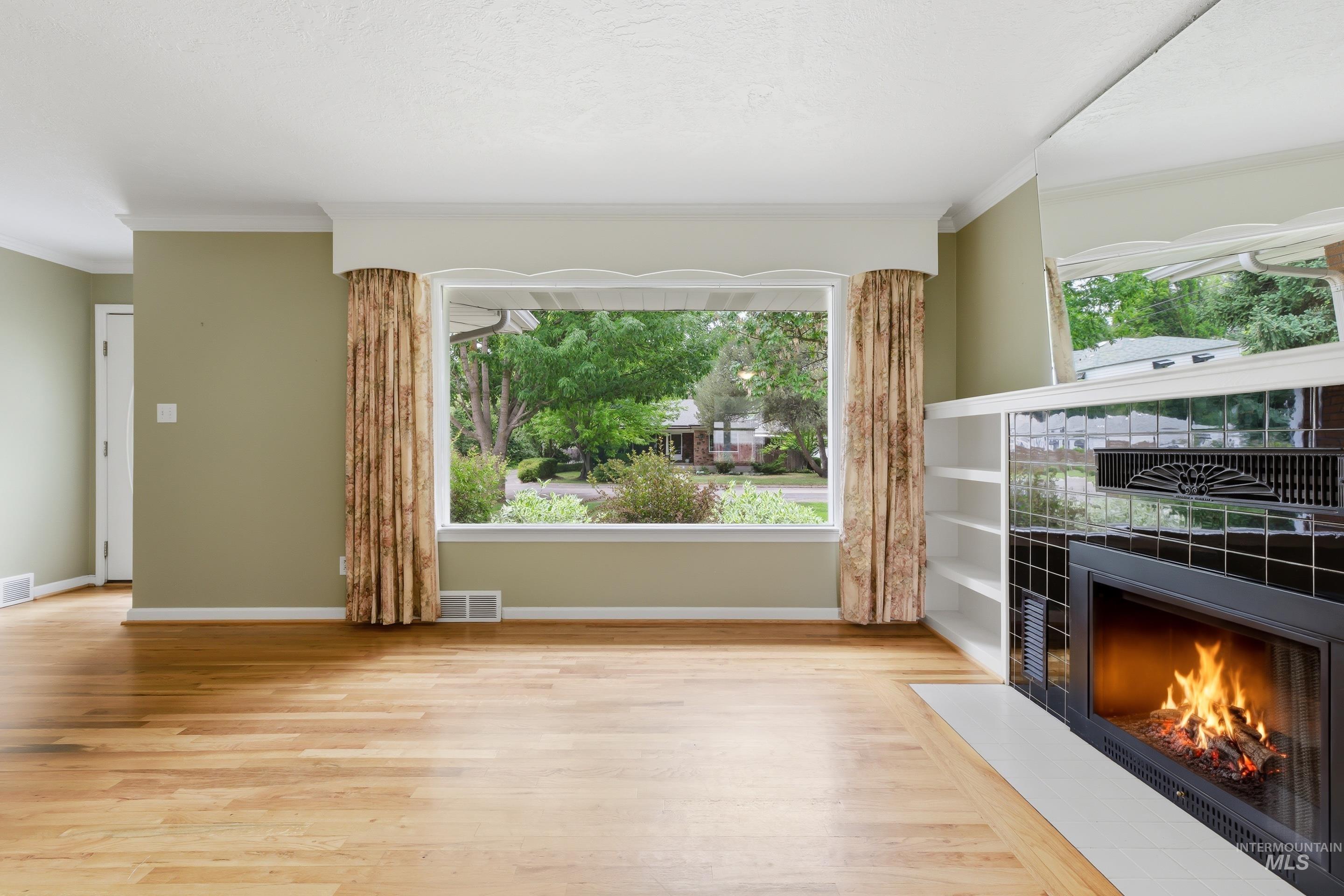 Living area with wood-finish flooring, a large picture window, and a built-in fireplace with black tile surround and integrated shelving