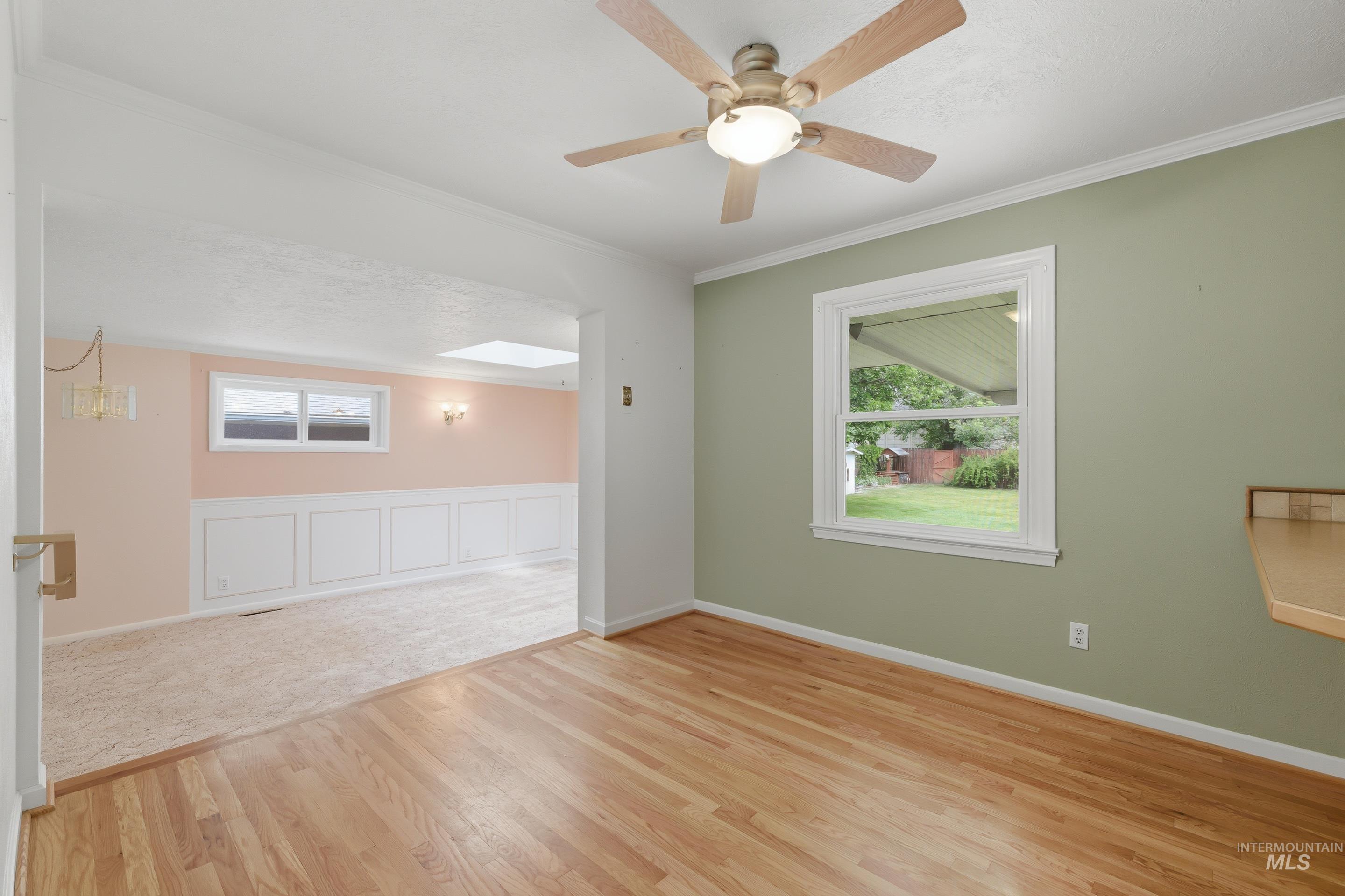 Hardwood flooring in a room with a ceiling fan light fixture and a window providing natural light