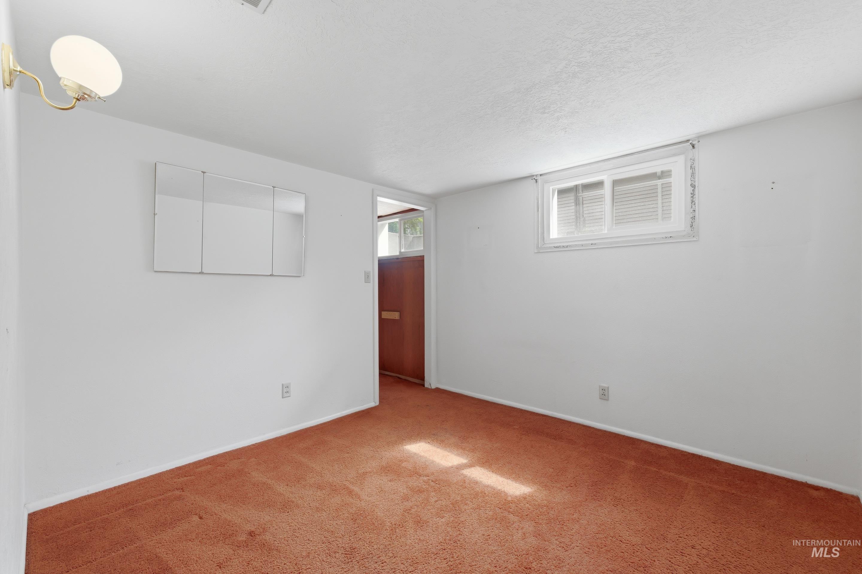 Carpeted room featuring white walls, a single window with blinds, and a built-in wall sconce