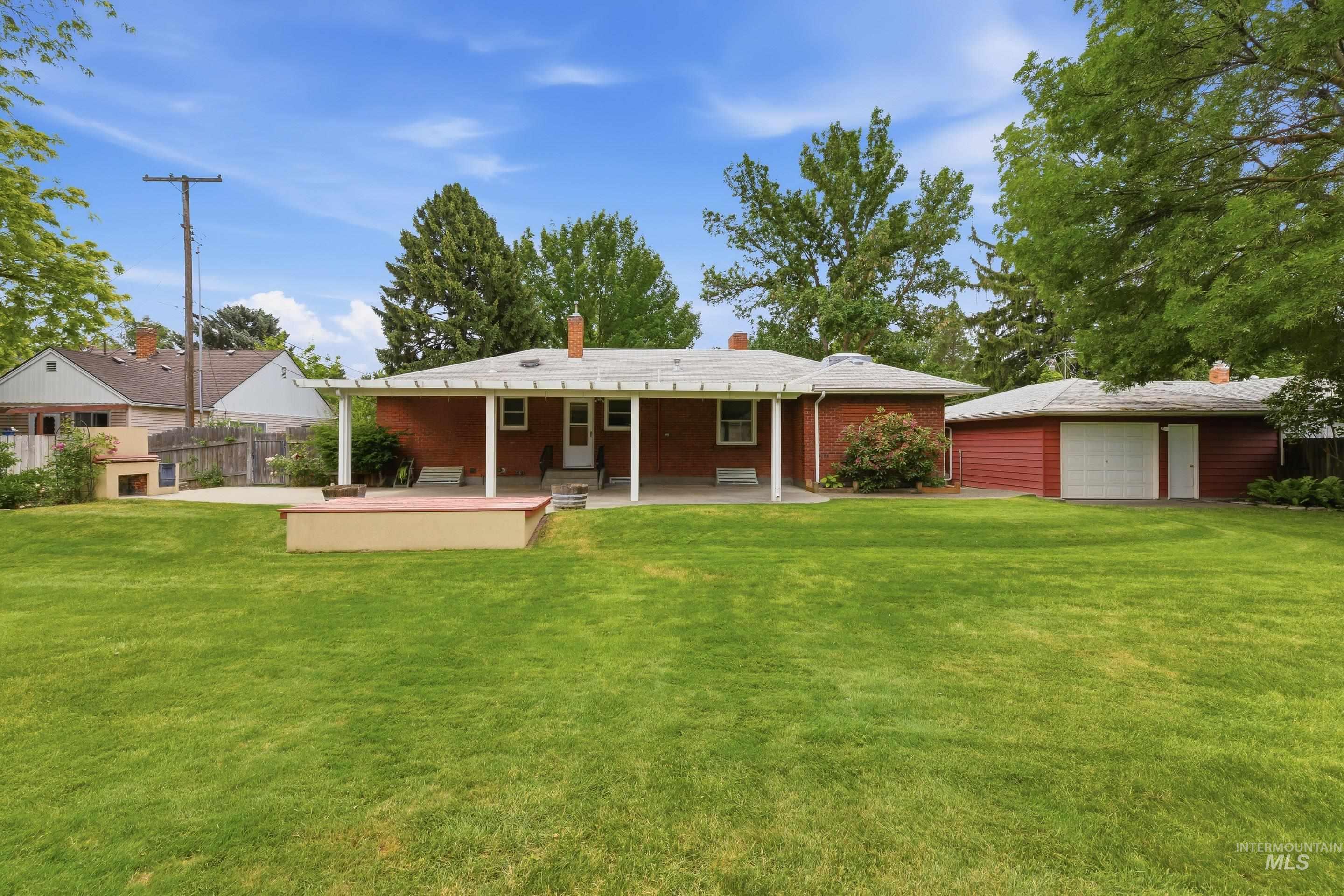 Expansive green lawn with a red brick ranch-style home featuring a covered patio with white columns and a separate two-car garage