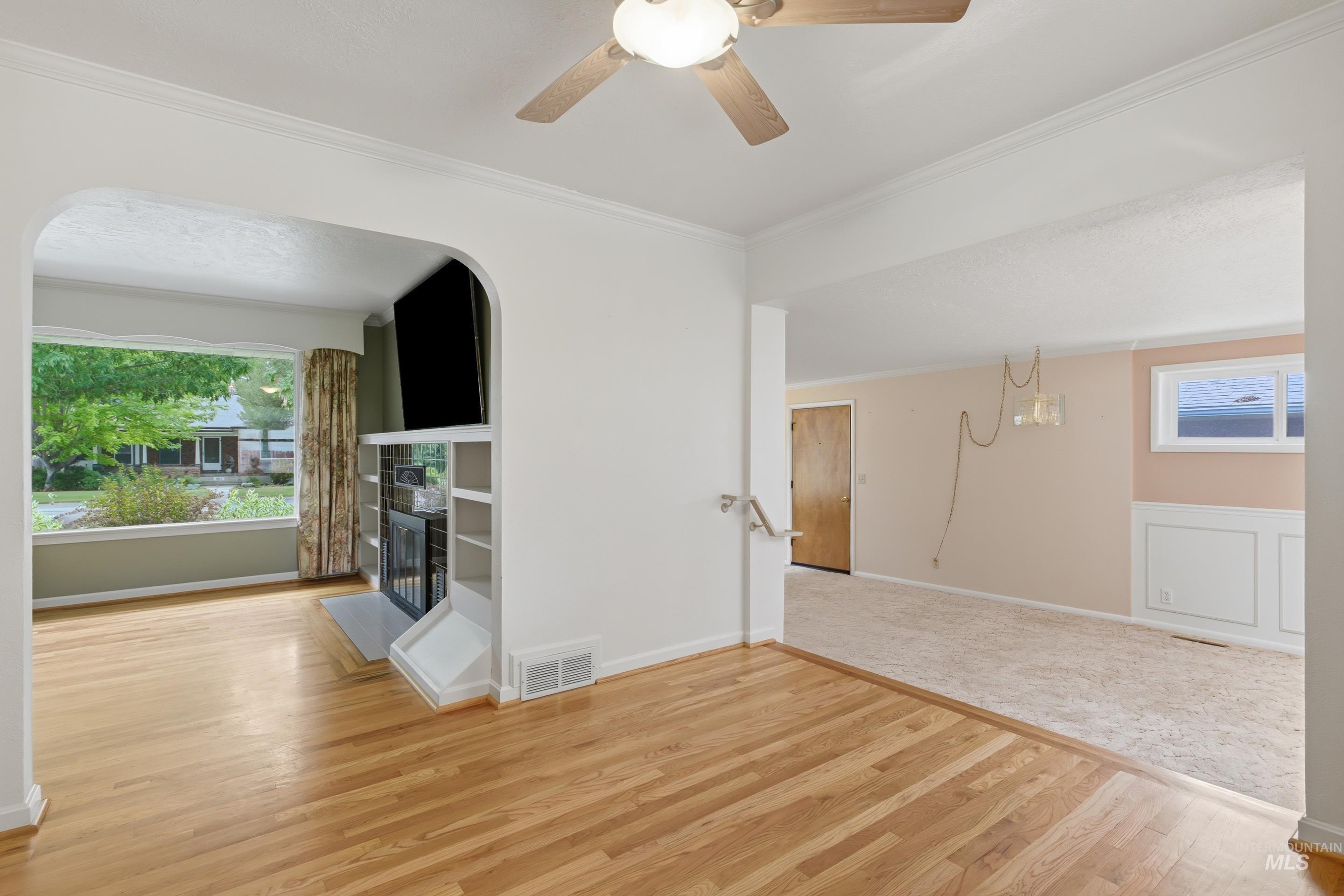 Hardwood flooring extending into an arched entryway, featuring a built-in fireplace with shelving, and crown molding