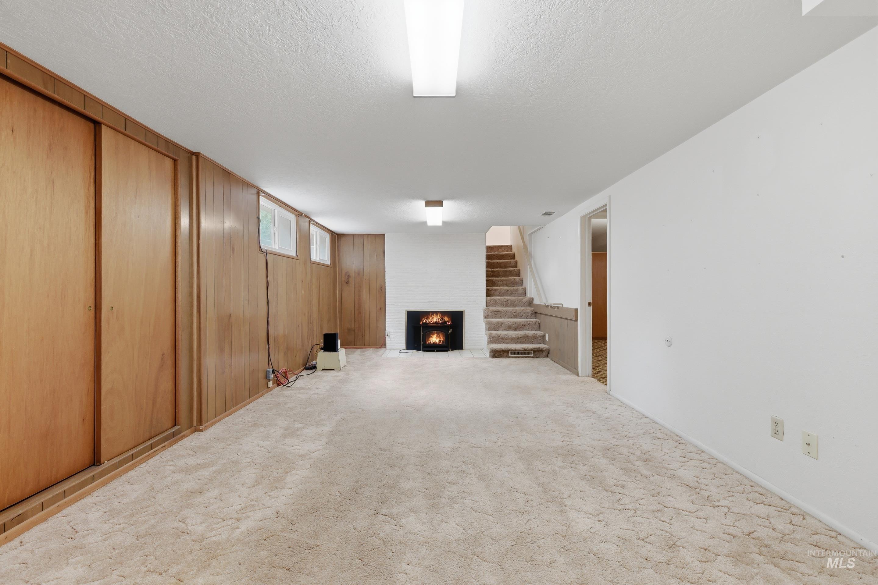 Spacious room featuring a built-in fireplace, paneled wall with sliding doors, white painted walls, and overhead lighting