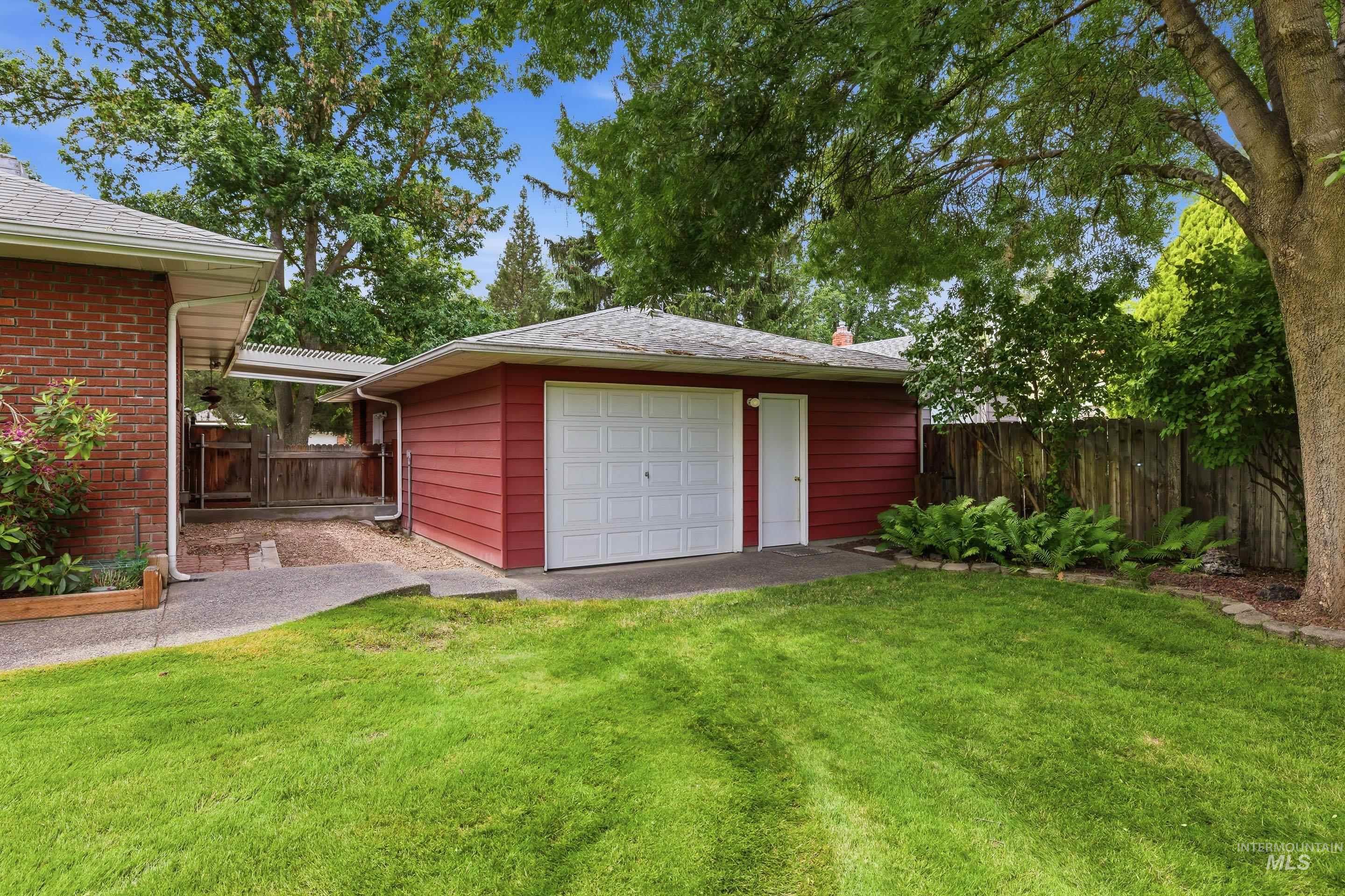 Detached garage with red siding and white overhead door, concrete driveway, and a separate entry door