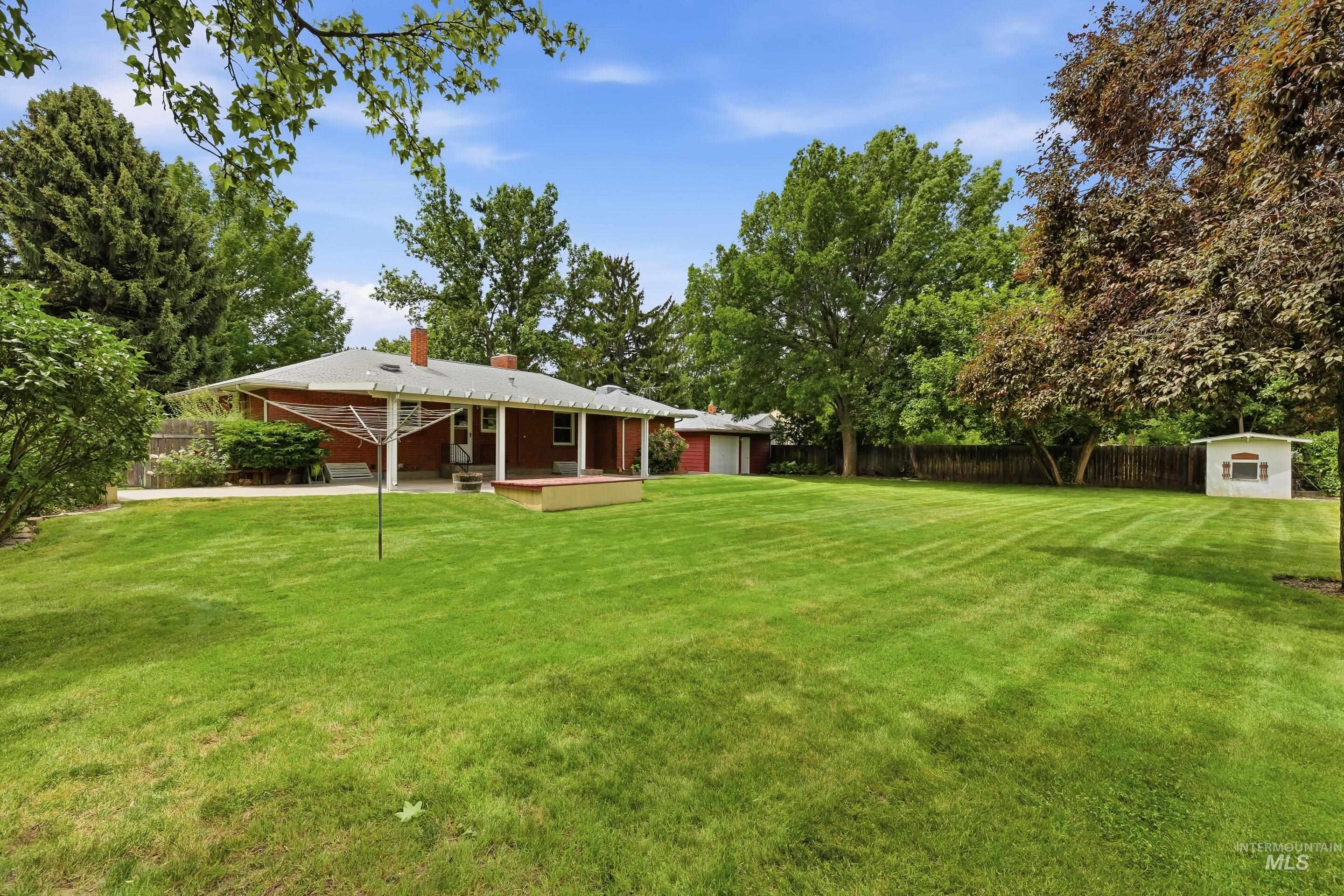 Expansive green lawn with mature trees, a red brick exterior, and a covered back porch with white columns