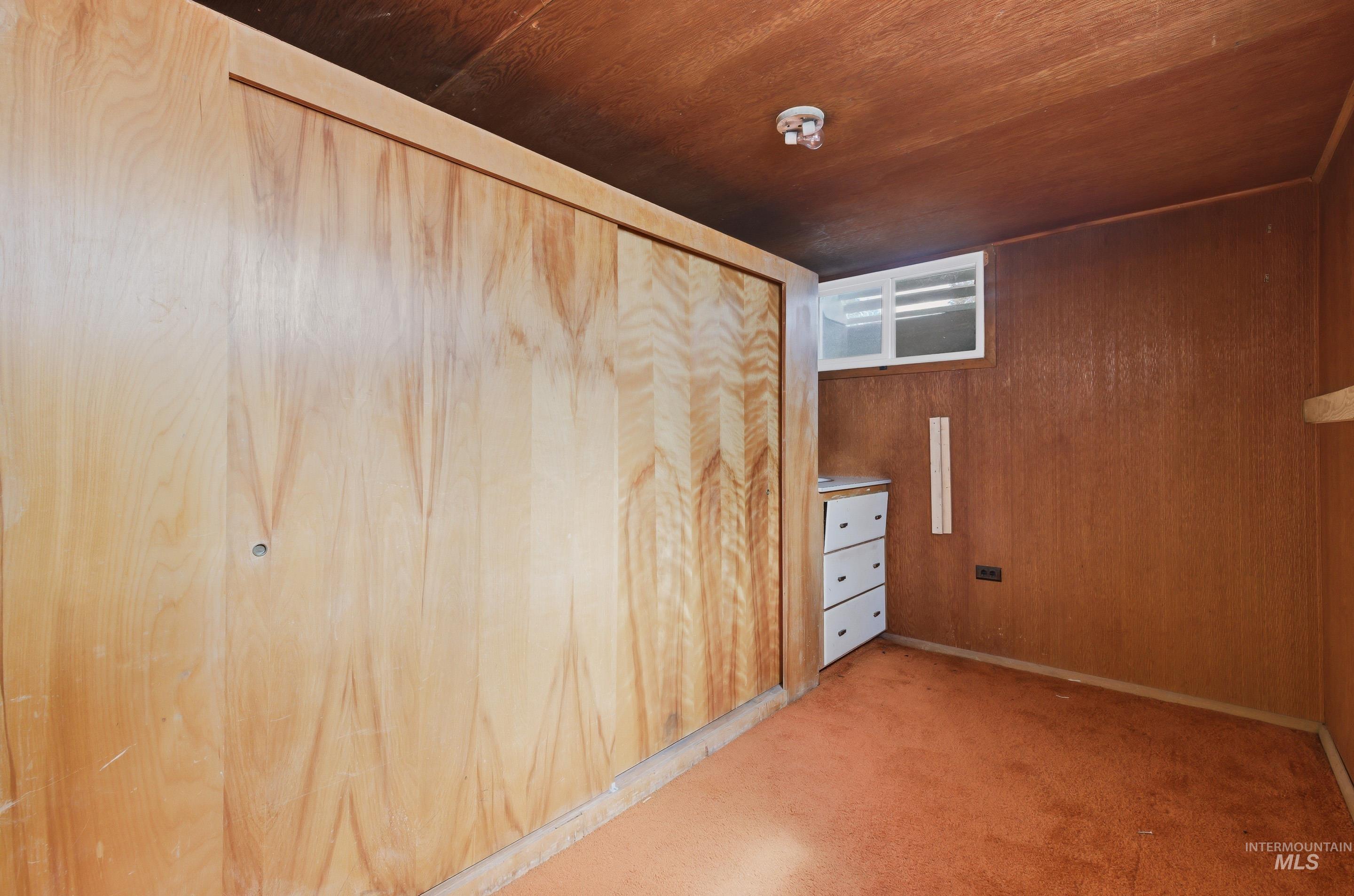 Wood-paneled wall with sliding closet doors, featuring a built-in three-drawer cabinet and a small, high-set window
