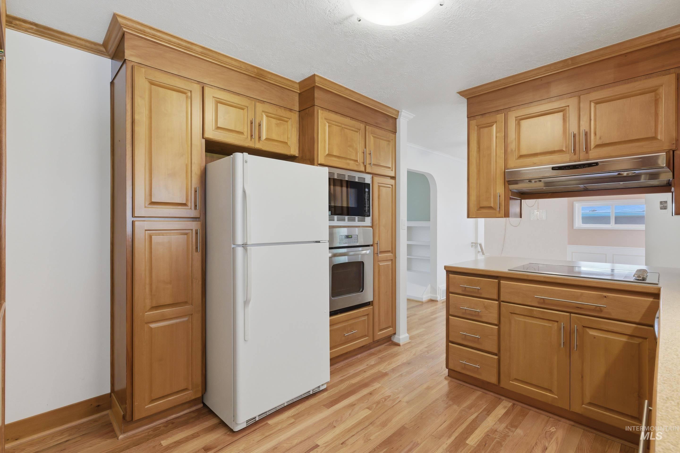 Kitchen featuring wood cabinetry, integrated stainless steel appliances, light-toned countertops, and wood-finish flooring
