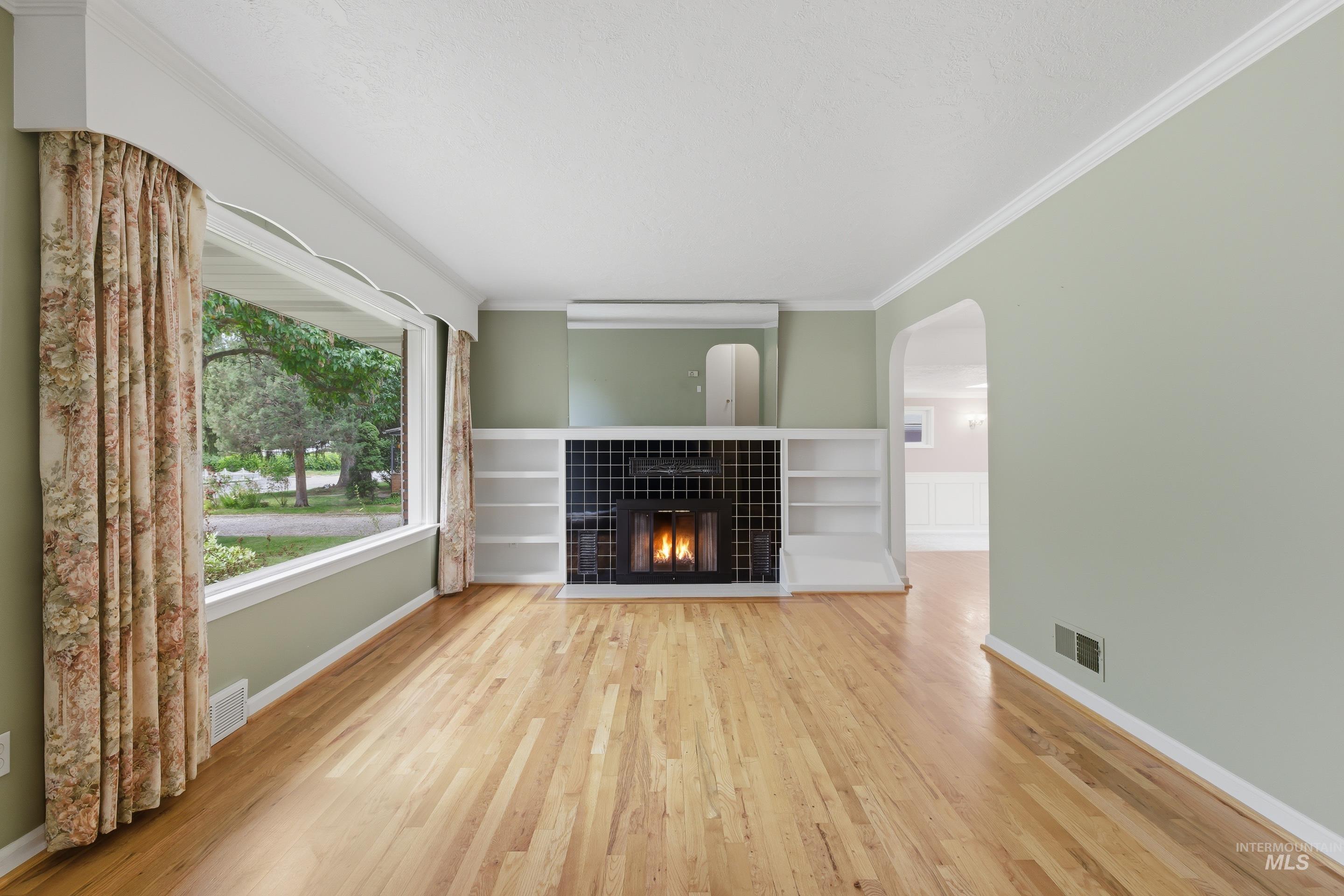 Living area featuring wood-finish flooring, a tiled fireplace with mantel, built-in shelving, and a large picture window