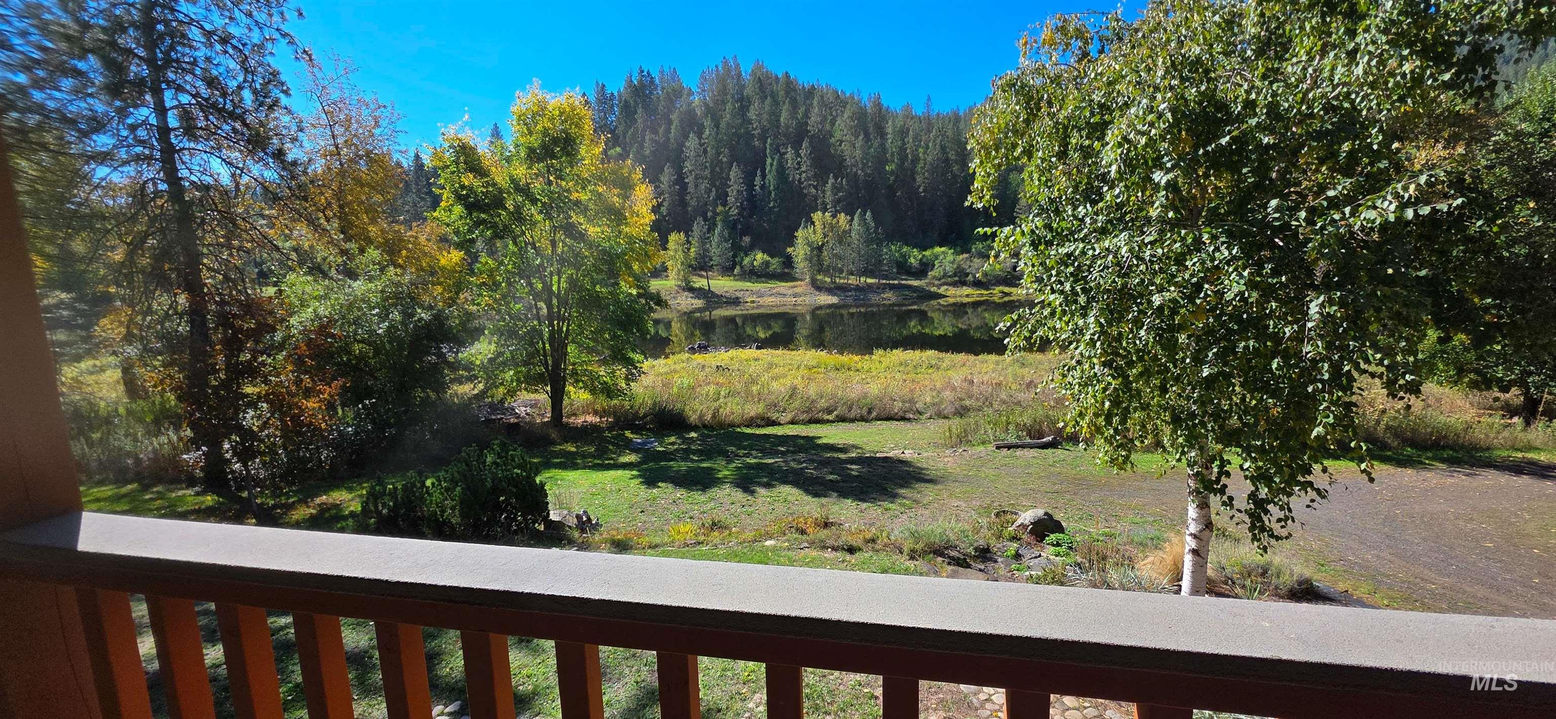 View of green lawn featuring a water view, a balcony, and a wooded view
