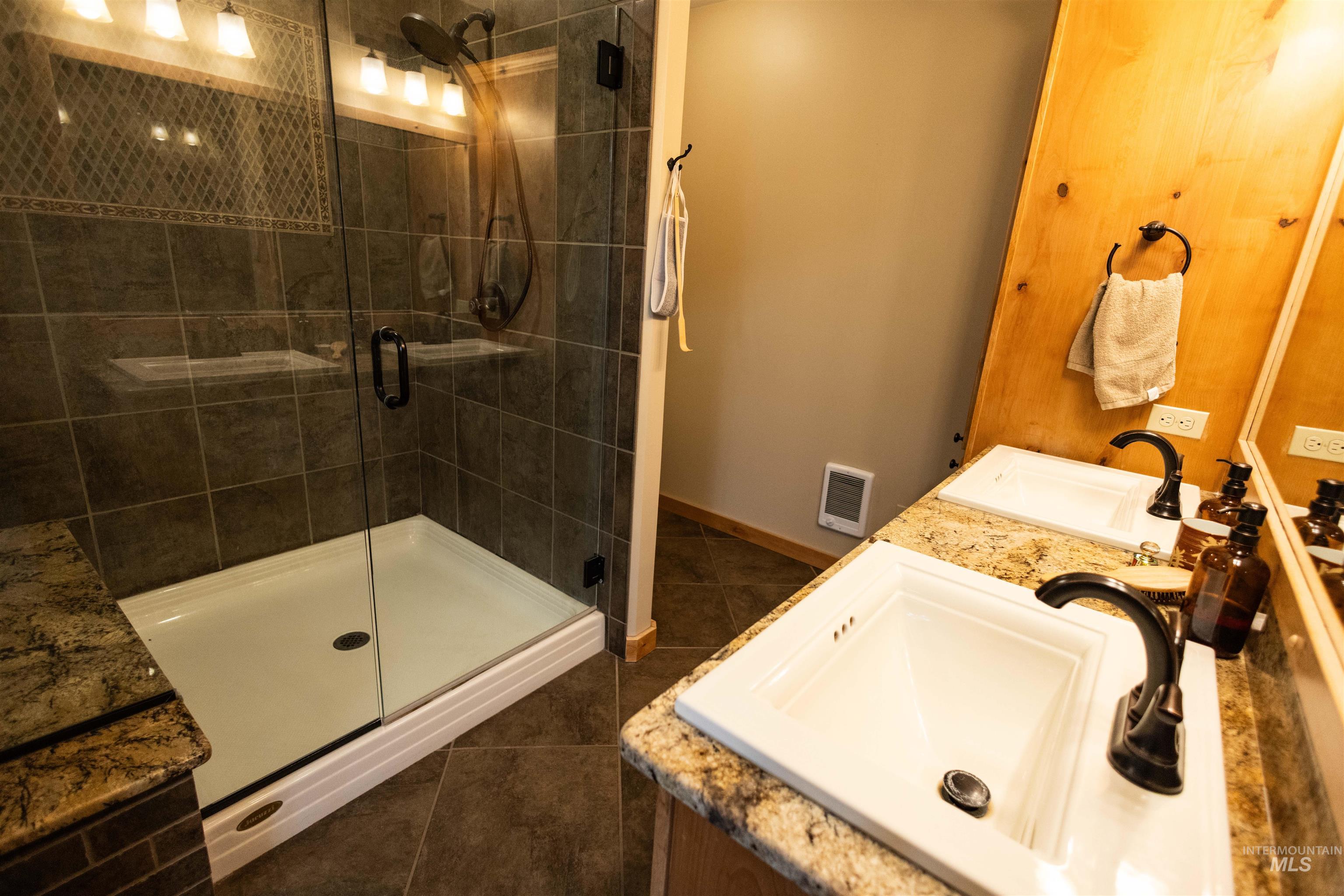 Full bath featuring double vanity, a shower stall, and dark tile patterned flooring
