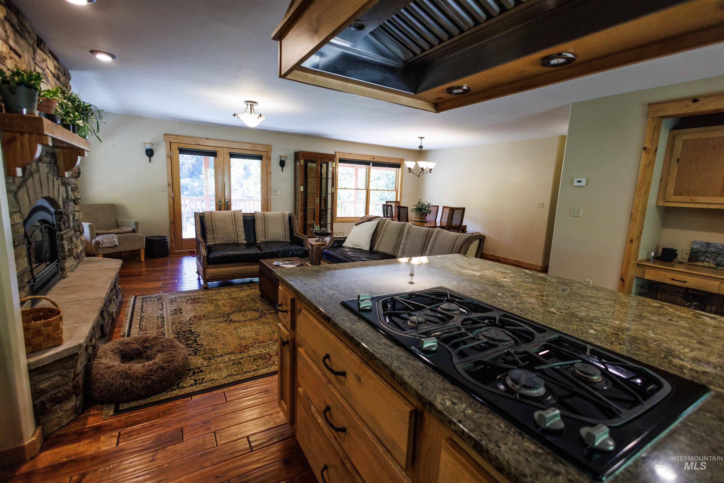 Kitchen featuring black gas cooktop, premium range hood, dark wood-type flooring, brown cabinets, and a stone fireplace
