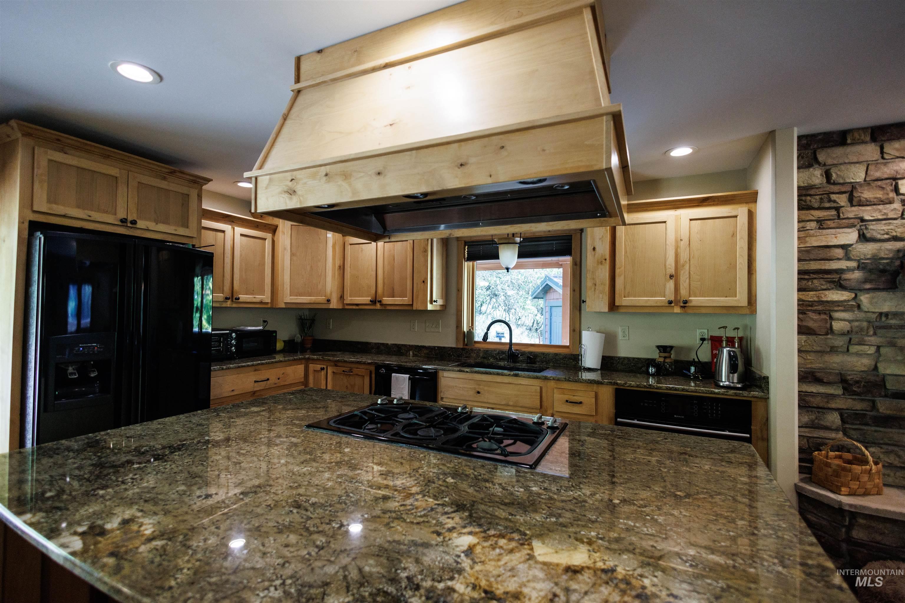 Kitchen with custom range hood, black appliances, dark stone countertops, recessed lighting, and a center island