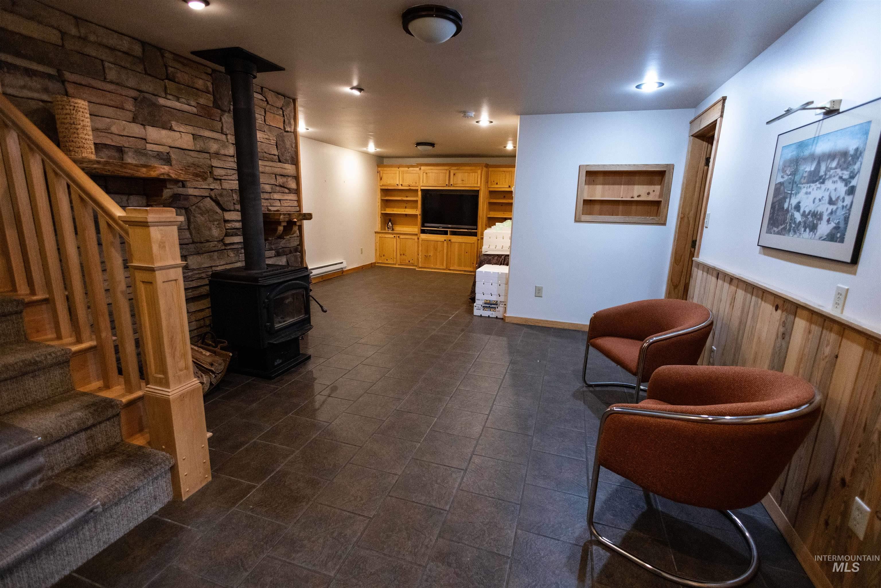 Living area with stairs, a wood stove, wood walls, a wainscoted wall, and a baseboard heating unit