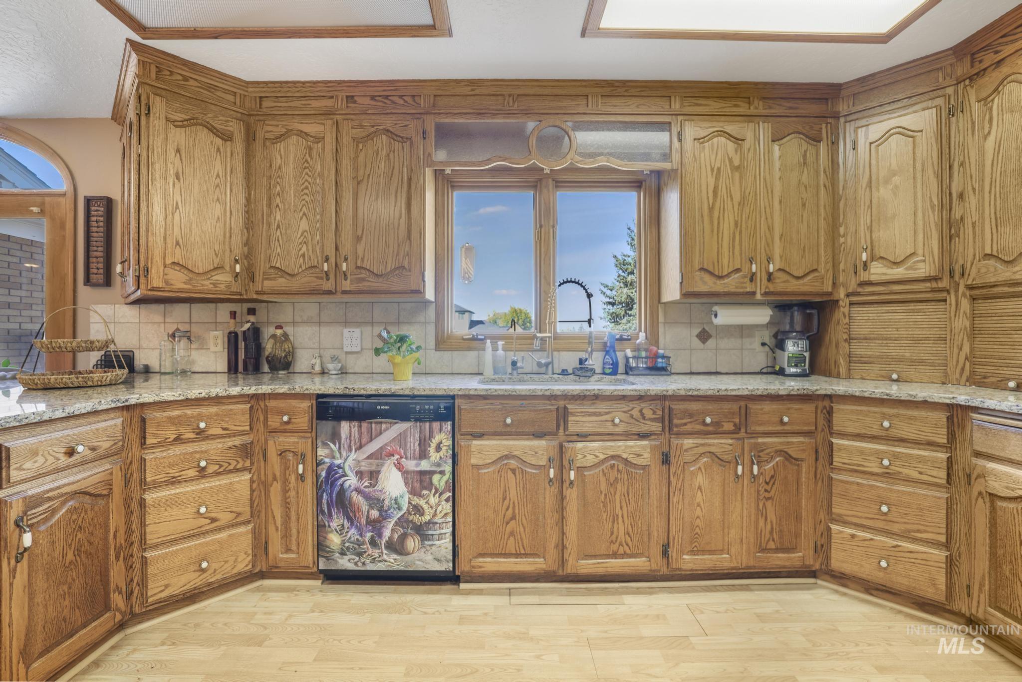 Kitchen with brown cabinetry, dishwasher, decorative backsplash, and light wood finished floors