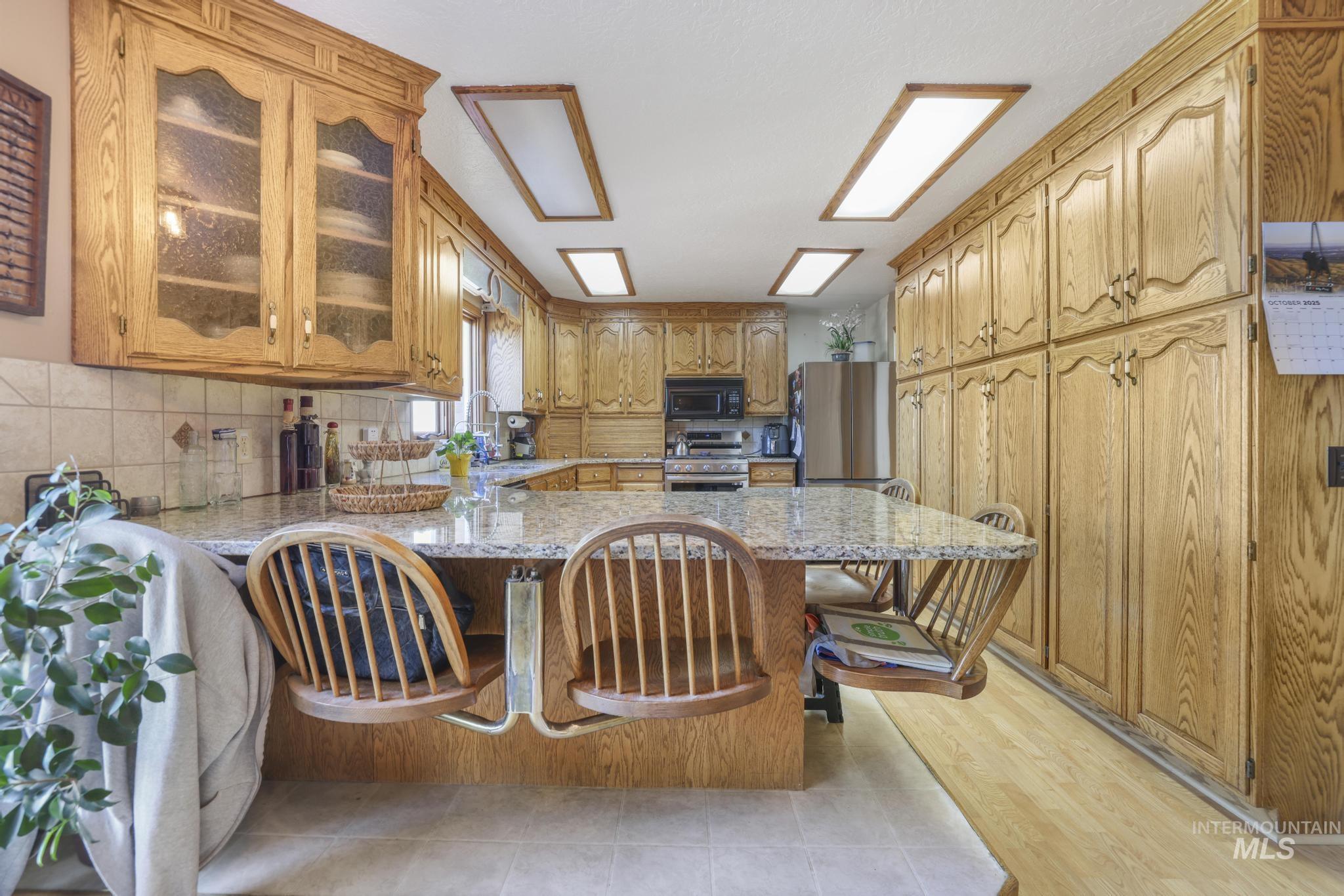 Kitchen with a breakfast bar area, light stone countertops, stainless steel appliances, brown cabinets, and a peninsula