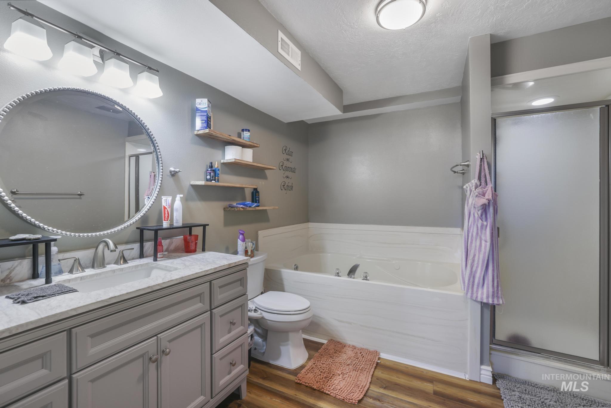 Full bath featuring vanity, a bath, a stall shower, dark wood-style flooring, and a textured ceiling