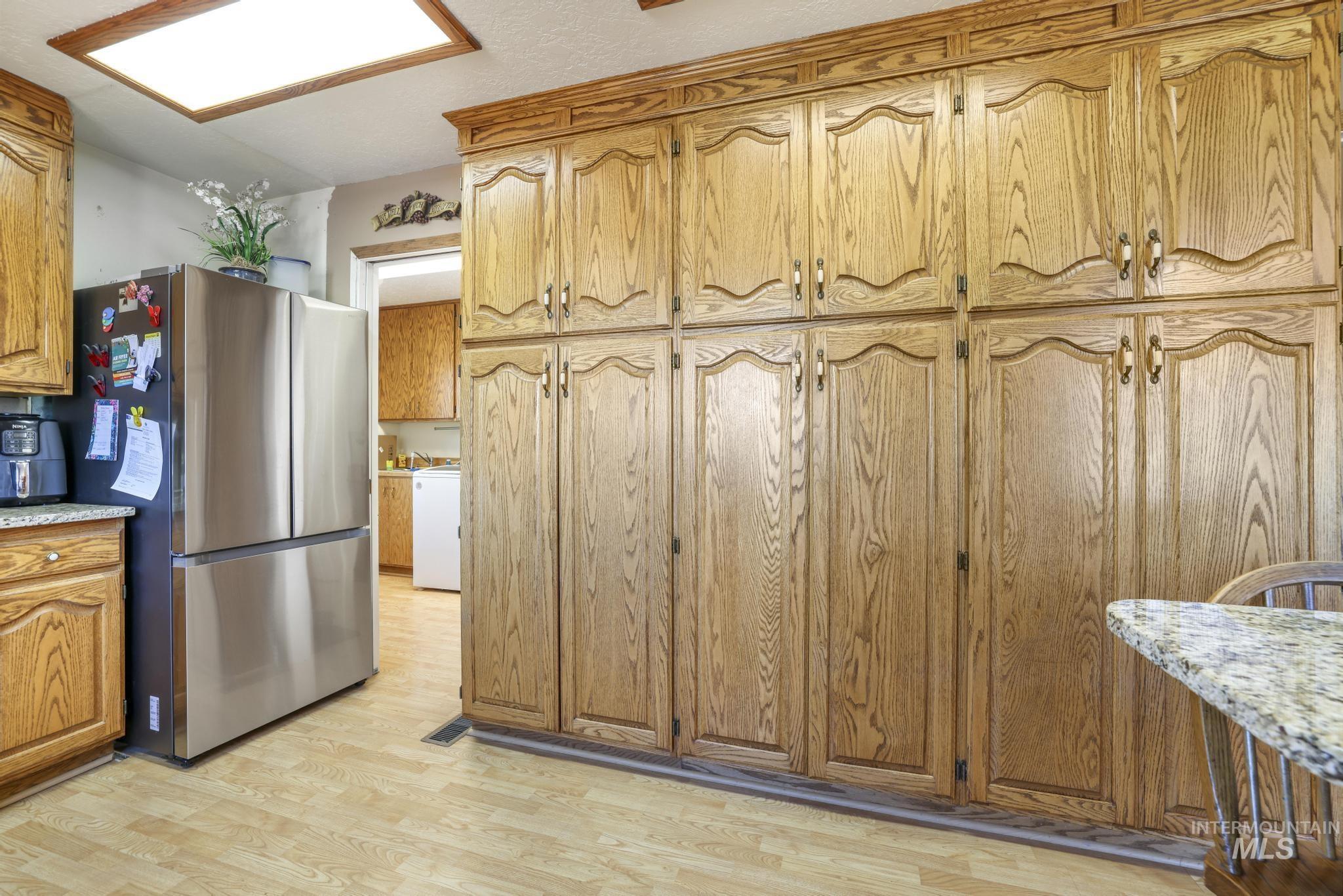 Kitchen with freestanding refrigerator, light wood-type flooring, light stone counters, brown cabinets, and washer / clothes dryer