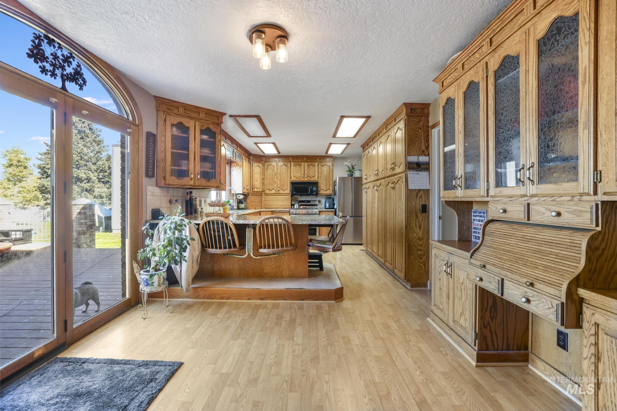Kitchen with glass insert cabinets, a peninsula, light wood-style floors, a breakfast bar, and brown cabinets