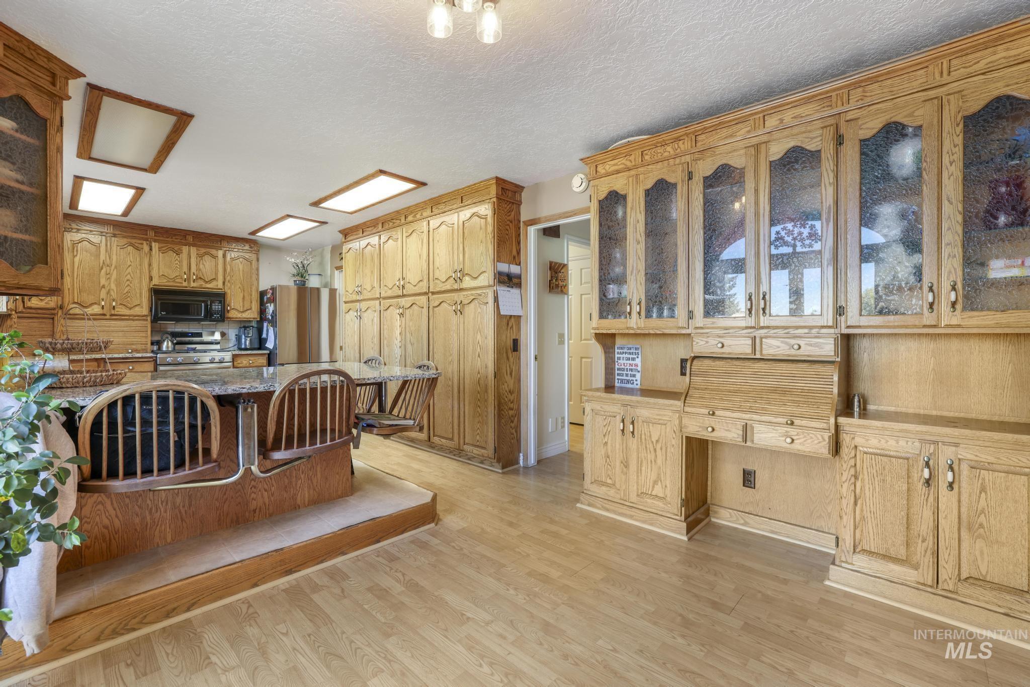 Kitchen with glass insert cabinets, a kitchen bar, light wood-style floors, stainless steel appliances, and a textured ceiling