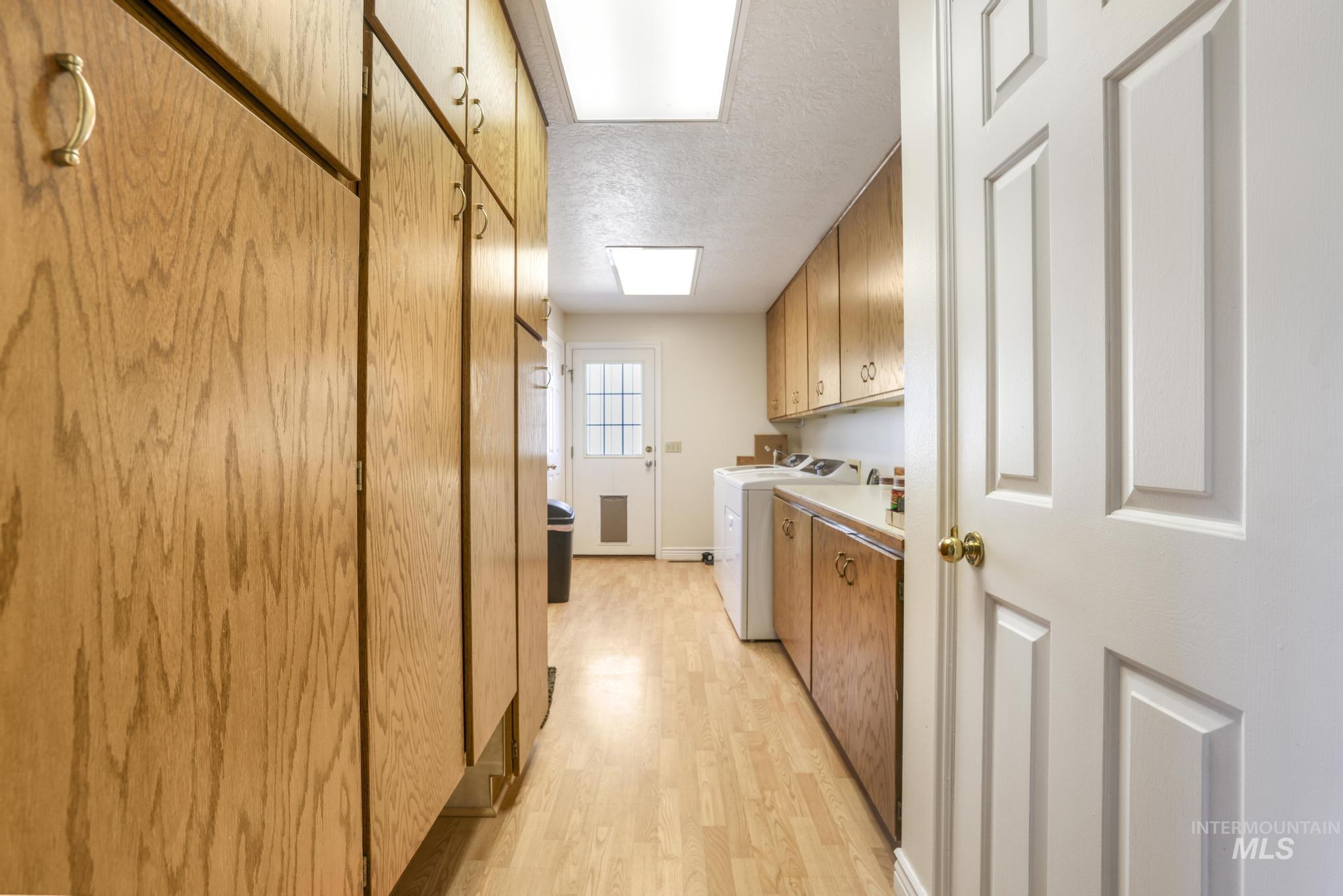 Laundry room with cabinet space, a textured ceiling, light wood finished floors, and washing machine and clothes dryer