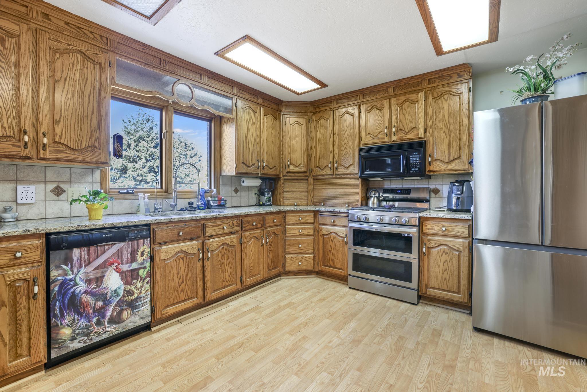 Kitchen with brown cabinets, black appliances, decorative backsplash, and light stone counters