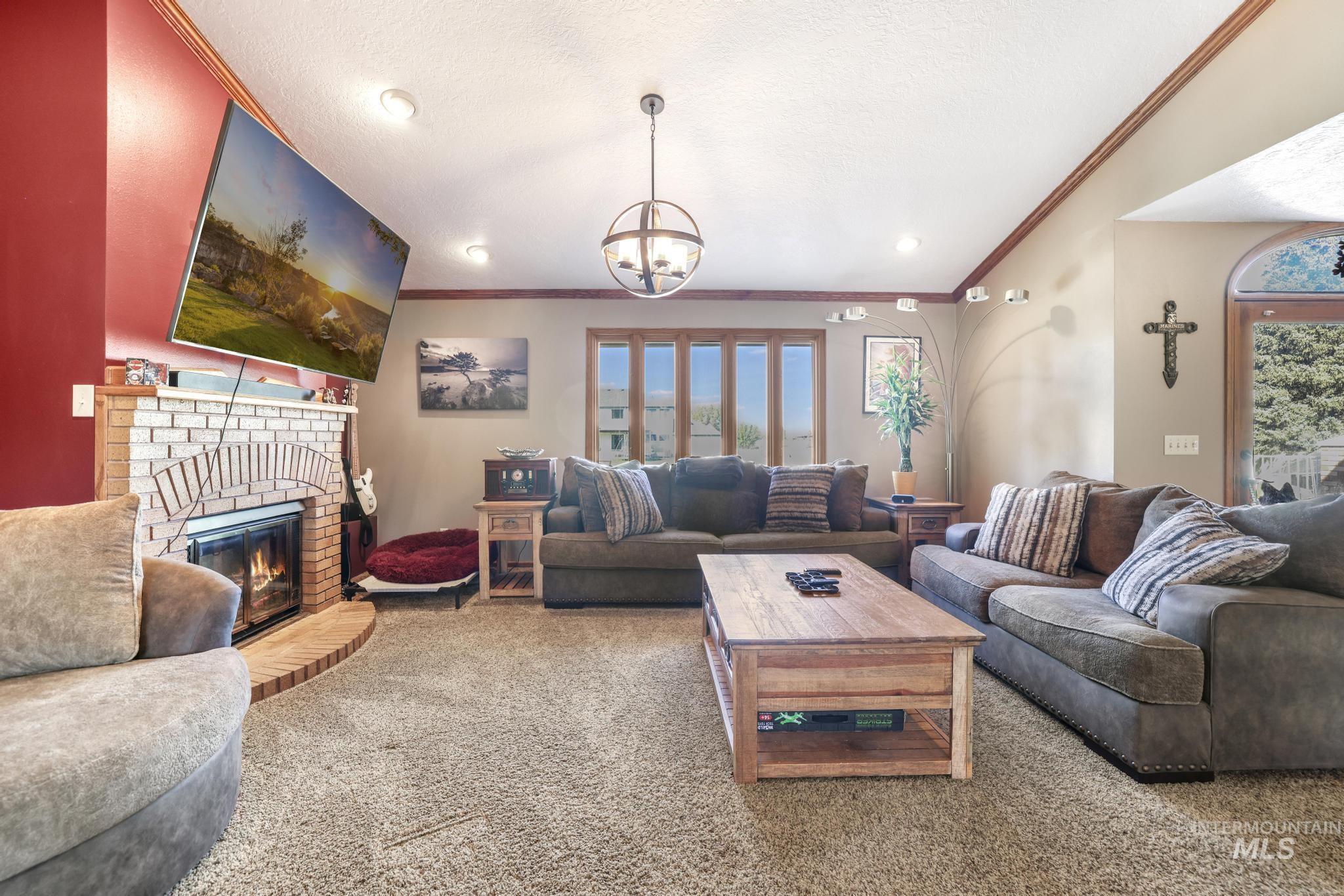 Living room with a brick fireplace, carpet floors, crown molding, a textured ceiling, and a chandelier