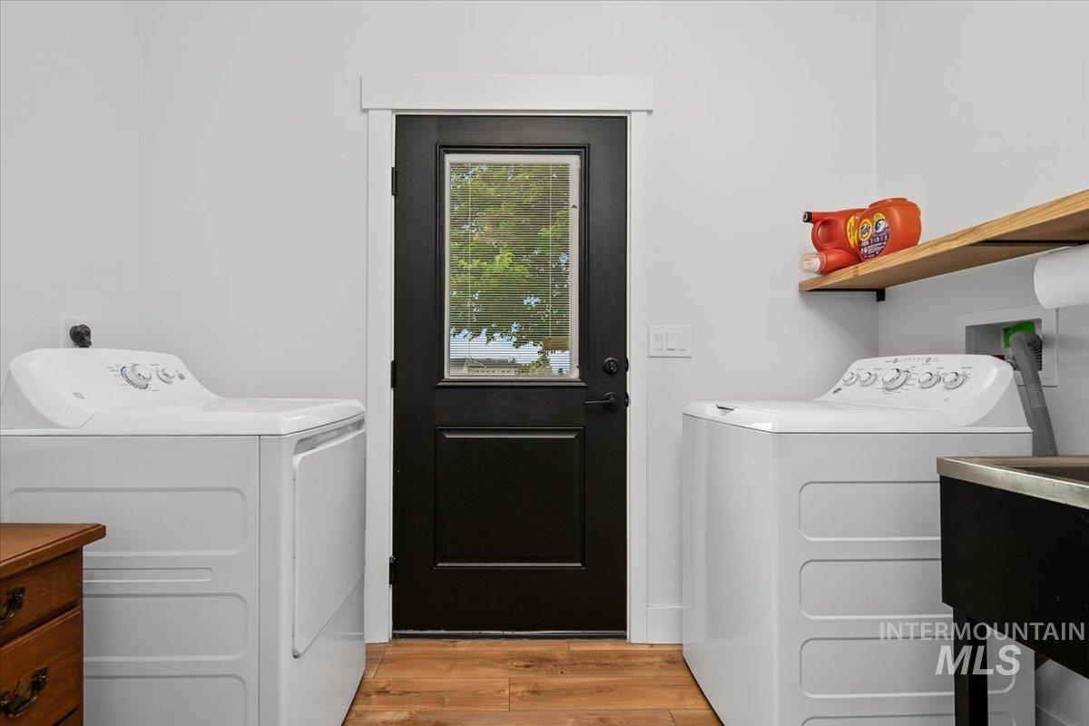 Washroom featuring washer and dryer and light wood-type flooring, outdoor access and utility sink.