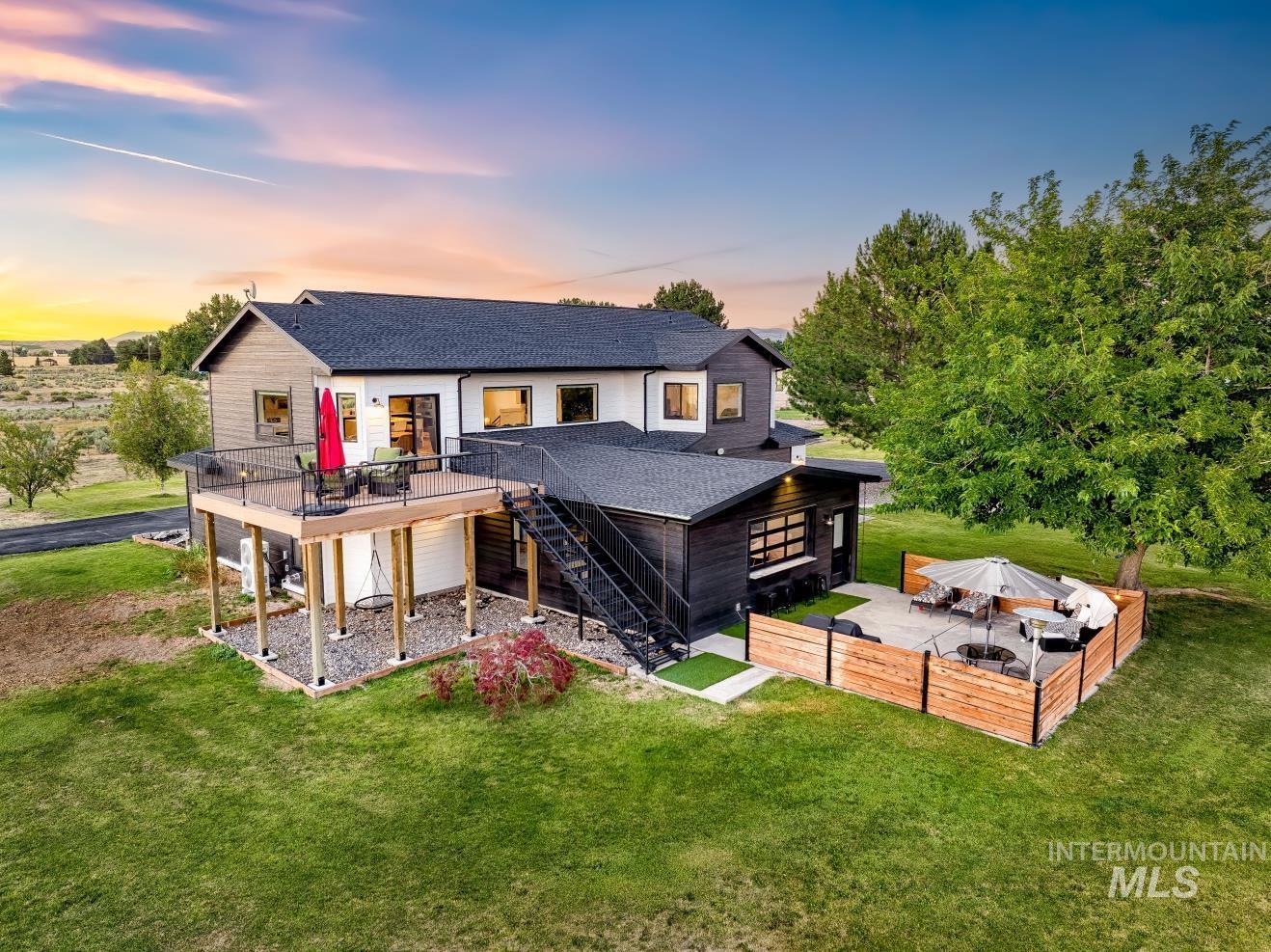 Sunset view of the back of house featuring a wooden deck, stairway, a shingled roof, and a lawn