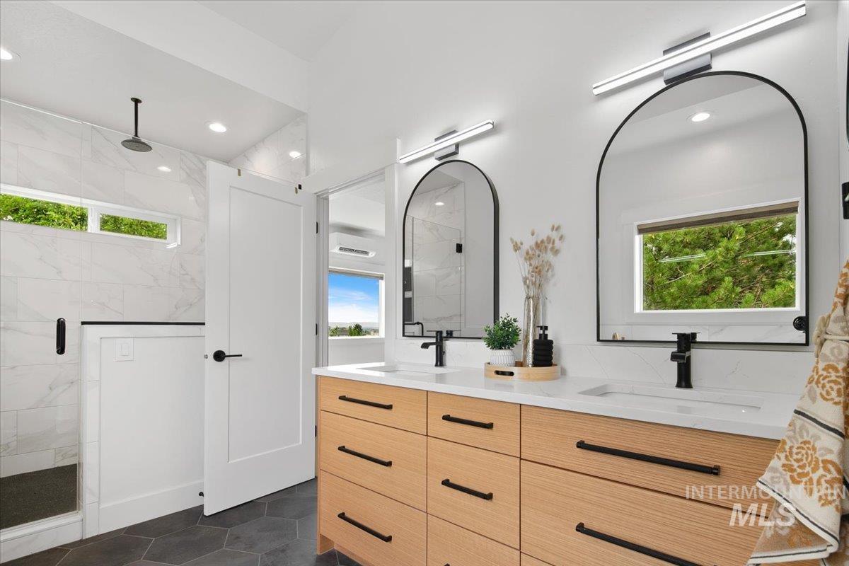 Full bath featuring double vanity, healthy amount of natural light, a marble finish shower, tile patterned floors, and recessed lighting