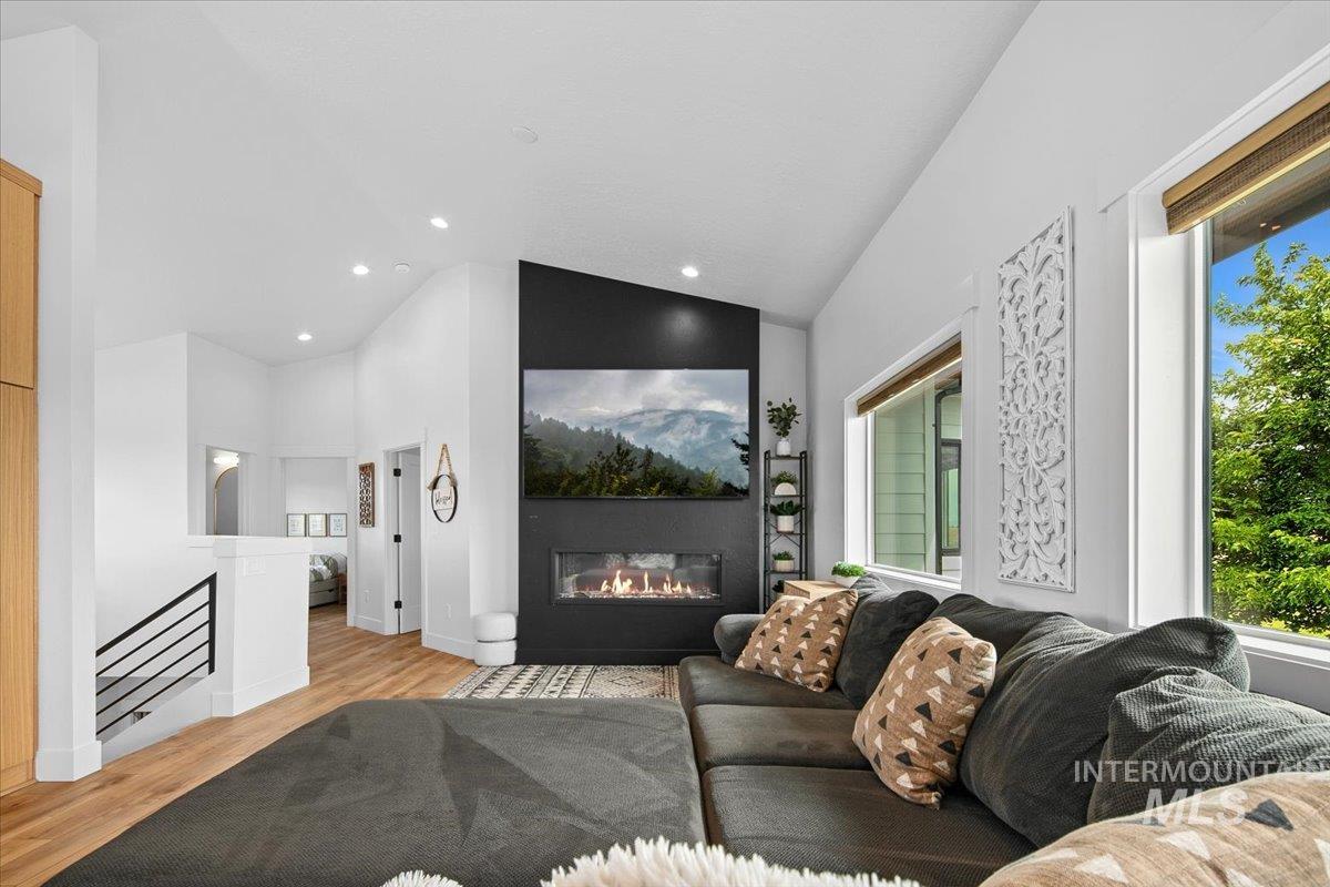 Living area with wood finished floors, a glass covered fireplace, recessed lighting, and high vaulted ceiling