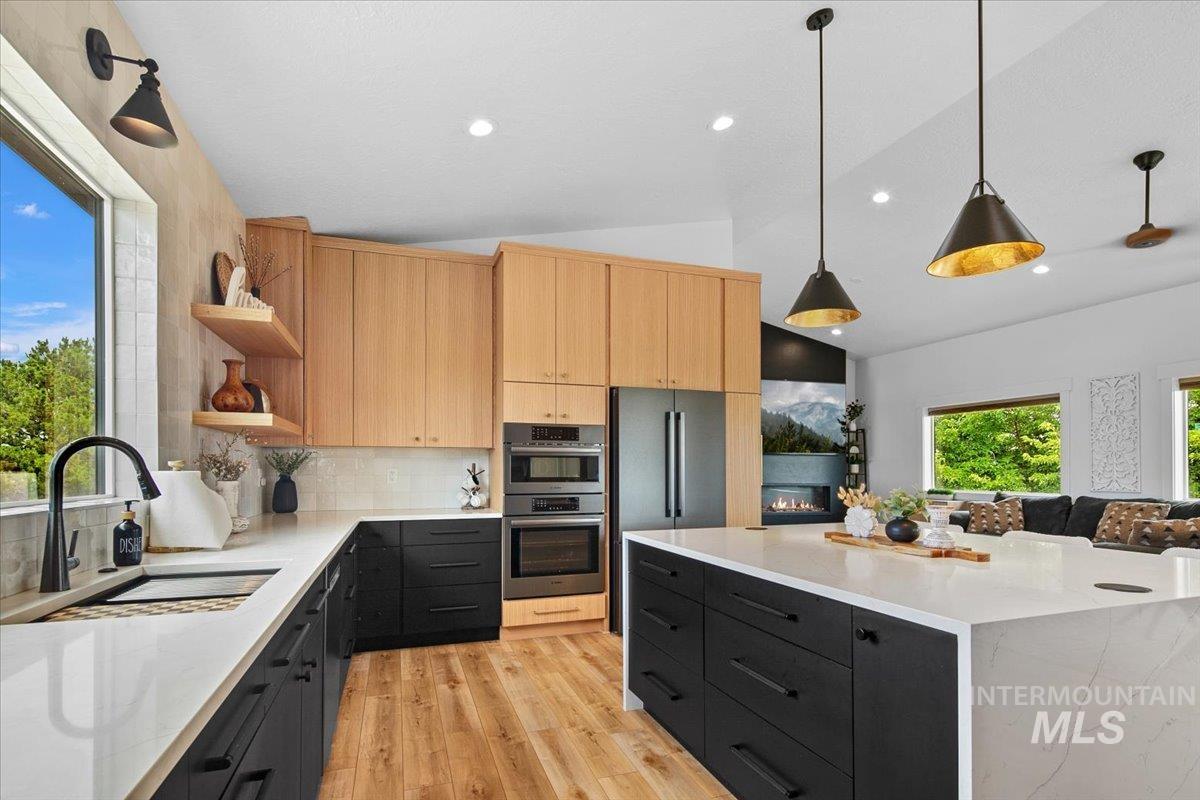 Kitchen with open shelves, lofted ceiling, light brown cabinets, dark cabinets, and light wood-style flooring