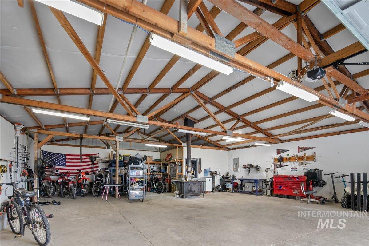 Garage featuring a workshop area, a wood stove, a garage door opener, and electric panel & Office area to back.