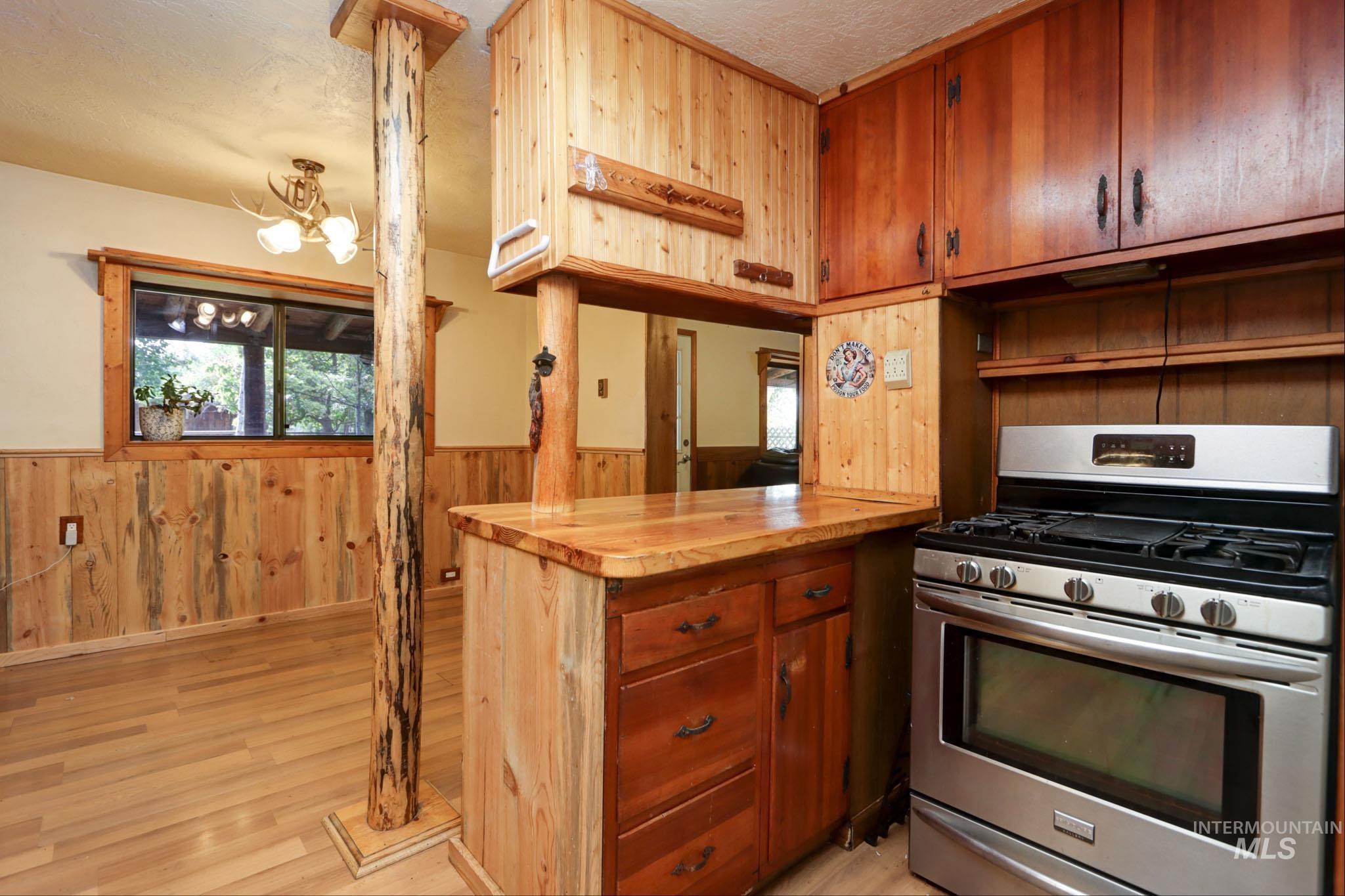 Kitchen with stainless steel gas stove, wooden walls, light wood finished floors, wainscoting, and plenty of natural light