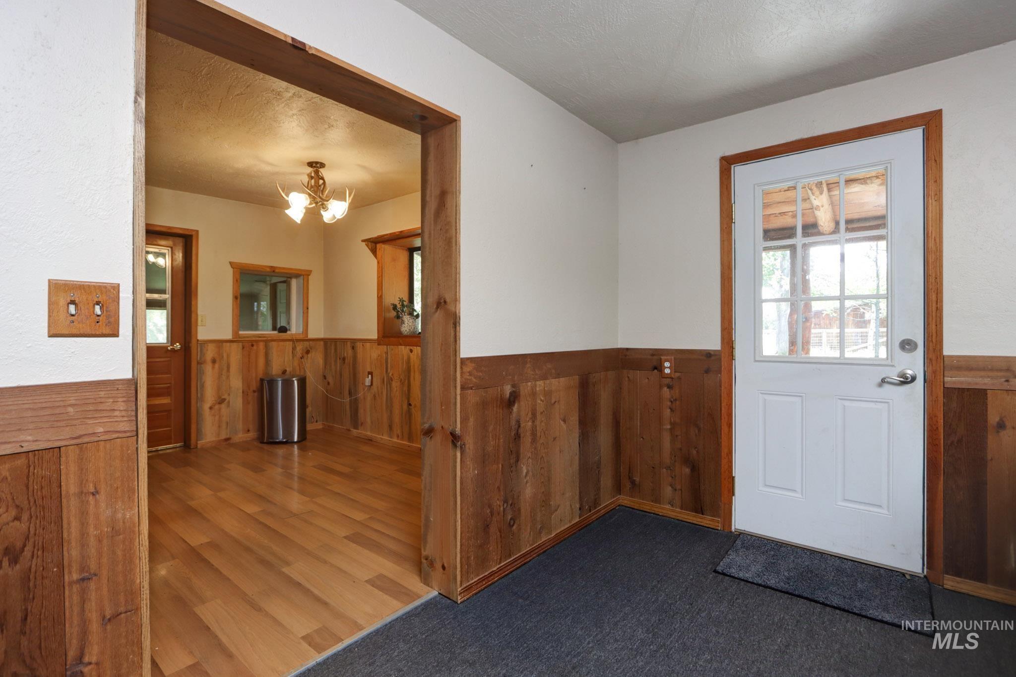 Doorway featuring wooden walls, wainscoting, wood finished floors, a chandelier, and a textured ceiling